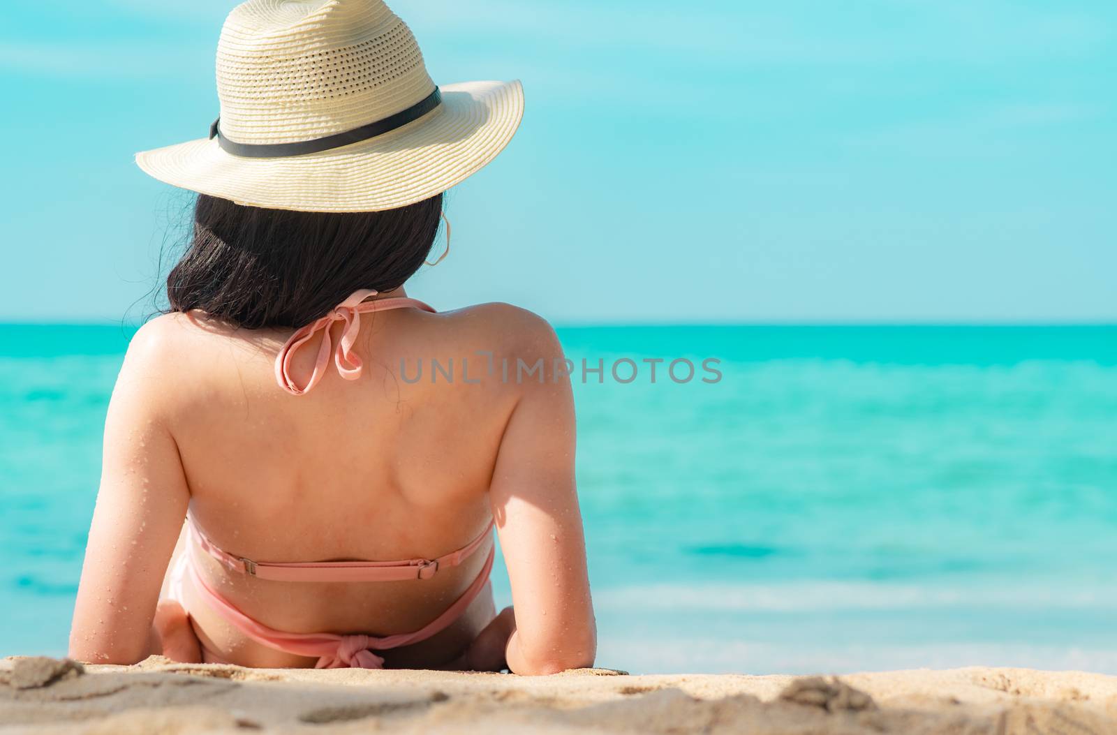 Back view of happy young Asian woman in pink swimsuit and straw  by Fahroni