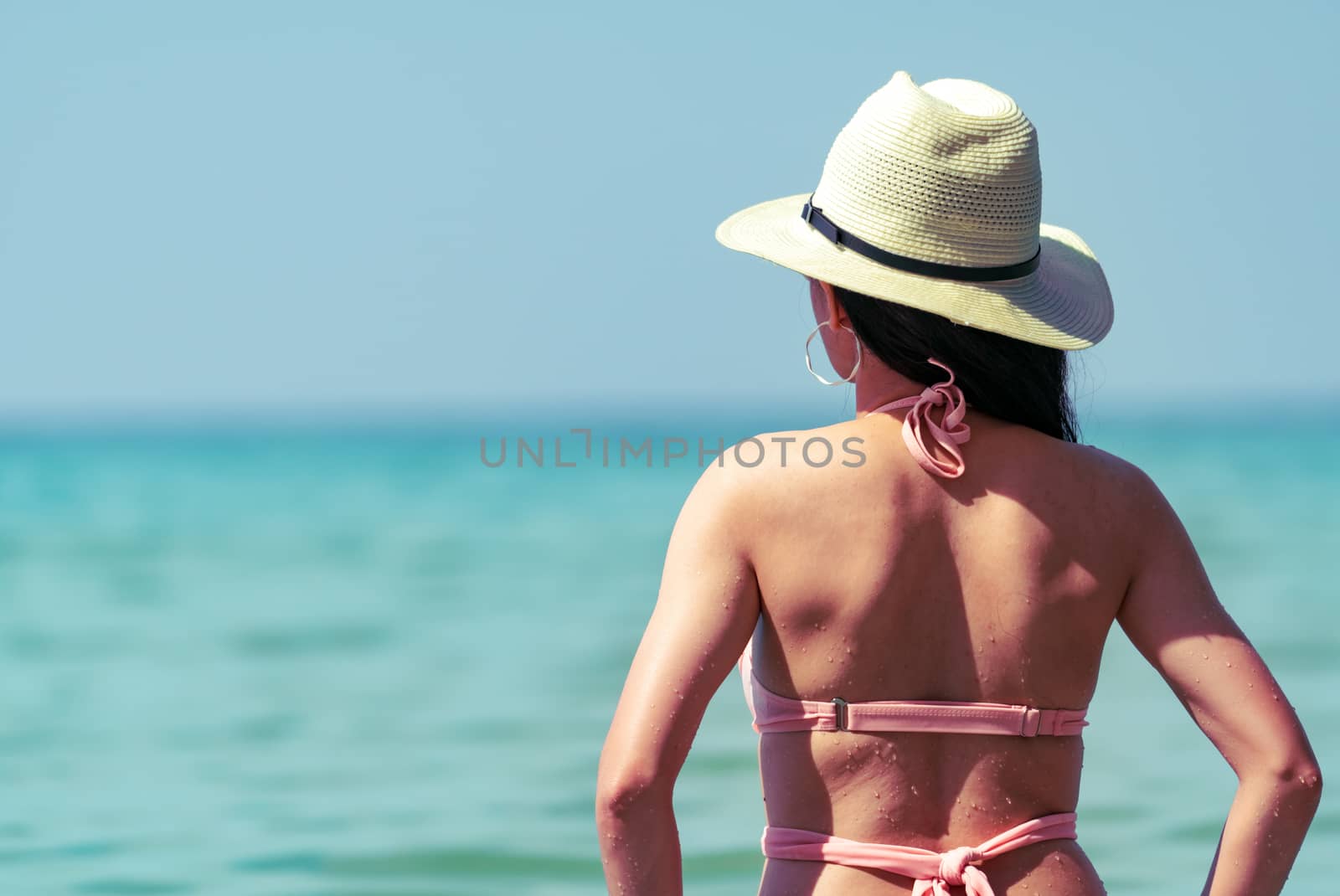 Back view of sexy young Asian woman wear pink bikini, straw hat, and sunglasses relaxing and enjoy holiday at tropical paradise beach. Girl in summer vacation fashion. Beauty sexy model. Summer vibes.