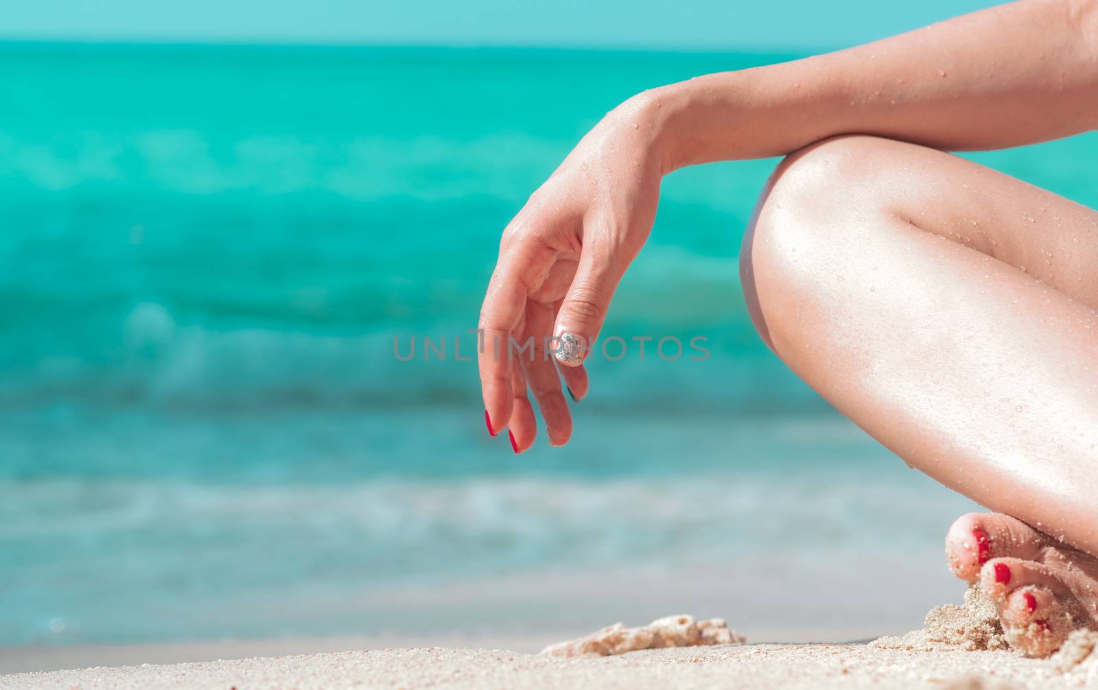 Closeup hand and leg of woman sit on sand beach at seaside with emerald green water. Happy young Asian woman relax and enjoy holiday at tropical paradise beach. Girl in summer vacation. Meditation. 