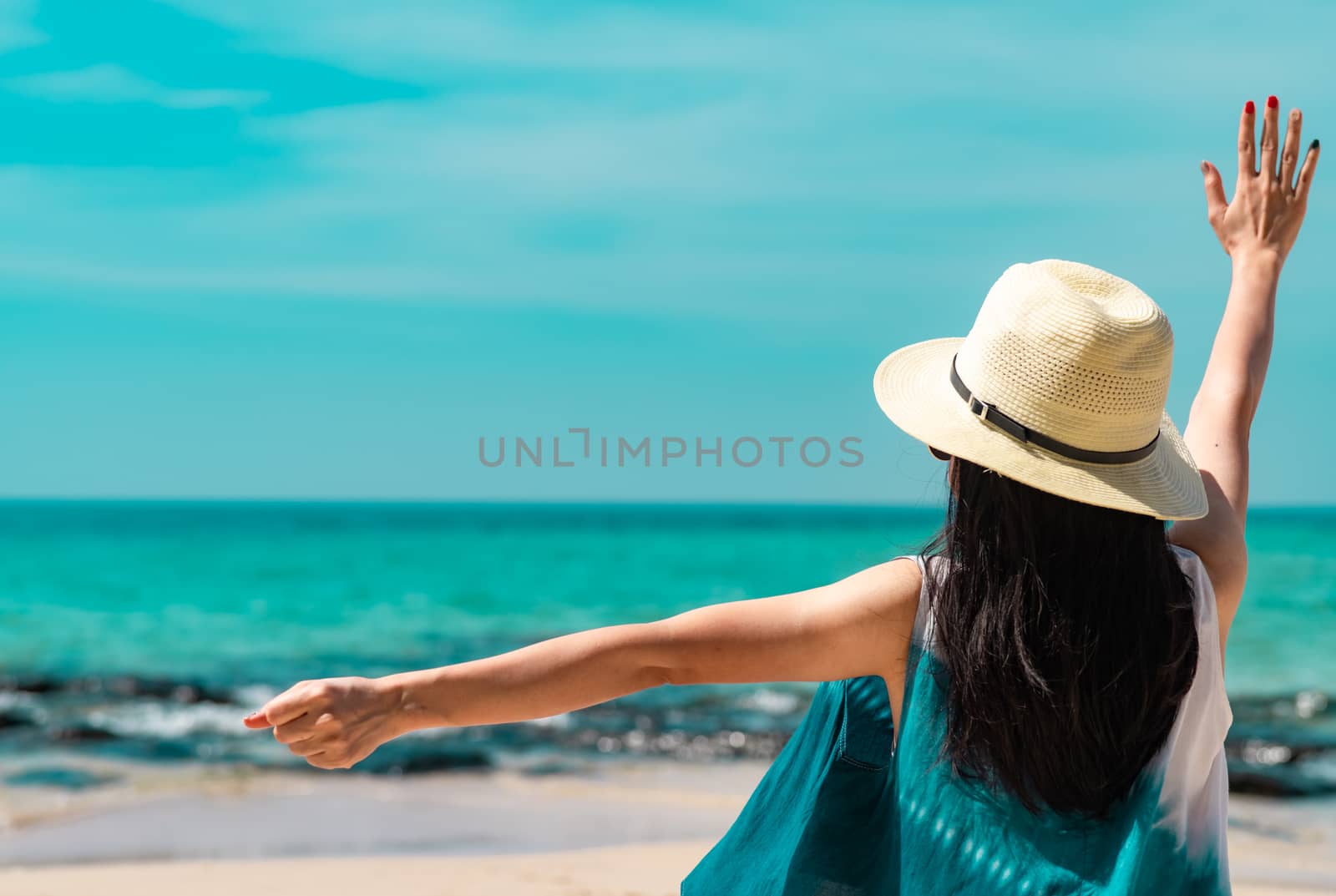 Happy young woman wear straw hat sit and raised hand at sand bea by Fahroni