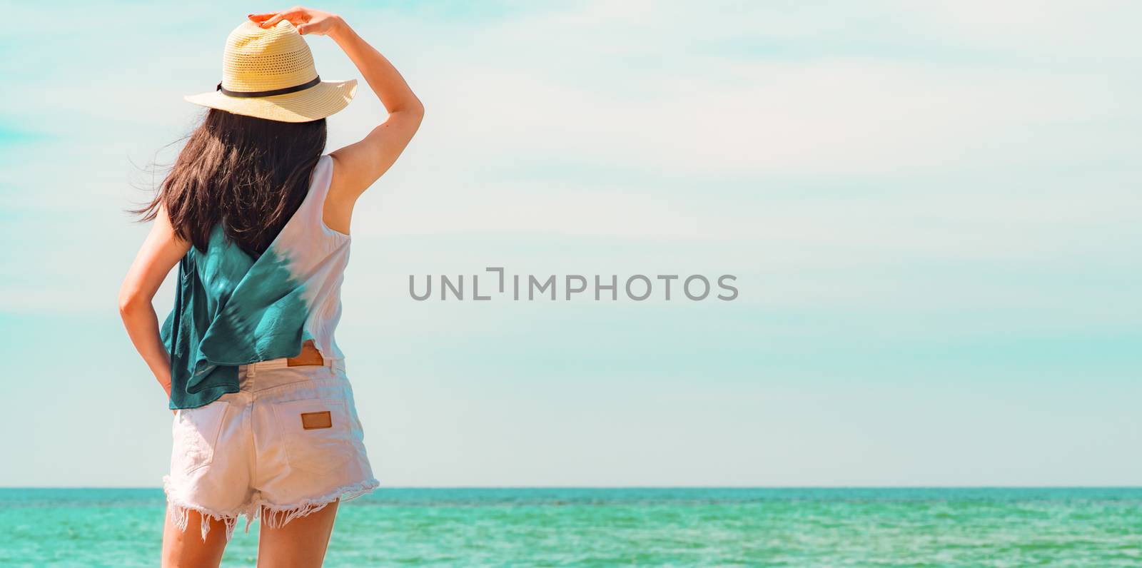 Happy young woman in casual style fashion and straw hat standing at sea beach. Relaxing and enjoy holiday at tropical paradise beach with emerald green sea water. Girl in summer vacation. Blue sky.