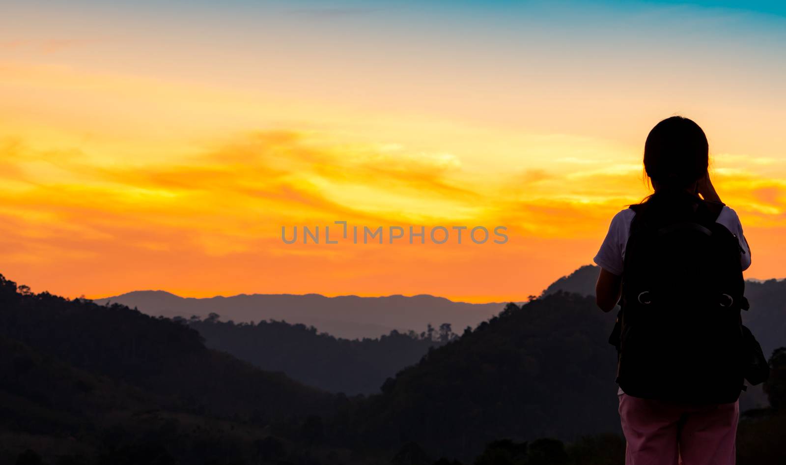 Back view of young woman watching beautiful sunset over mountain by Fahroni