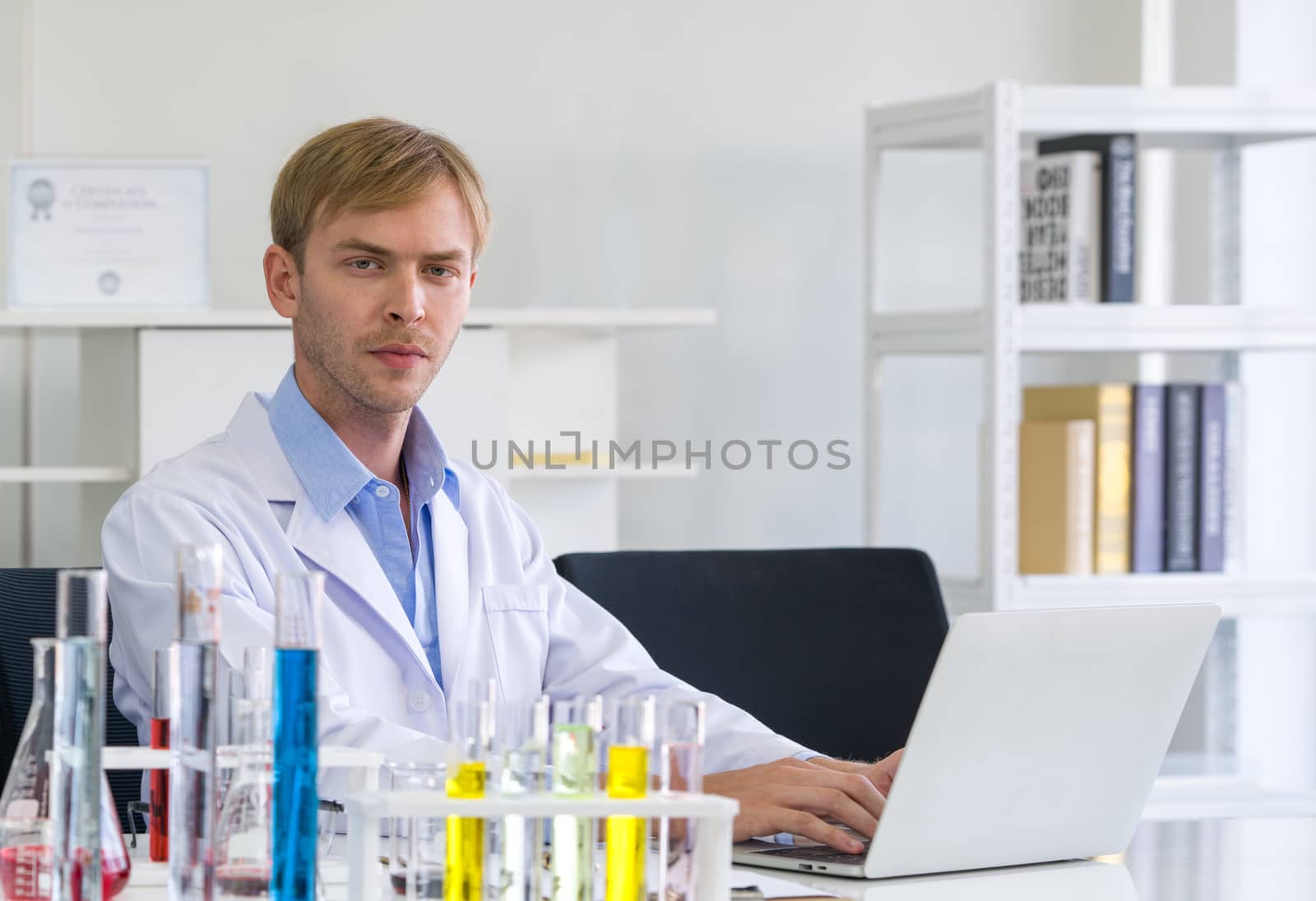 A young Brazilian scientist use computers to research chemical compounds on the internet. Working atmosphere in chemical laboratory. Test tubes filled with chemicals on the table.