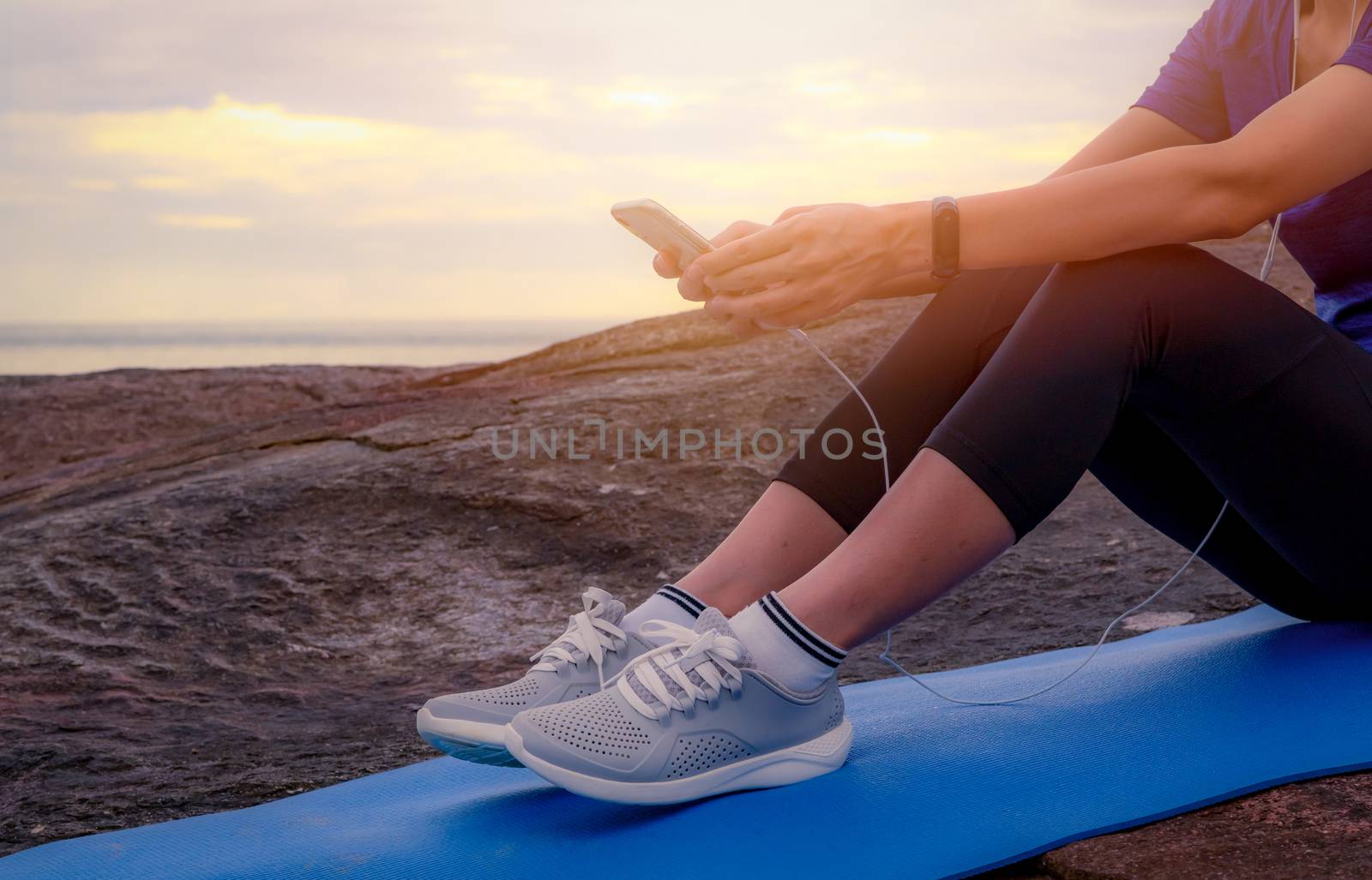 Woman sit and relax on yoga mat and listen to music via smartpho by Fahroni