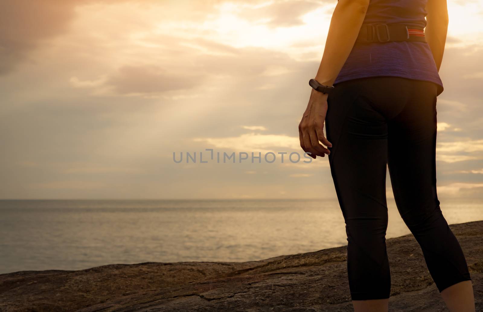 Adult Asian woman wear smart band standing at stone beach. Runner relax after running at tropical beach. Healthy lifestyle. Girl travel alone on summer vacation. Holiday at the coast of the ocean.