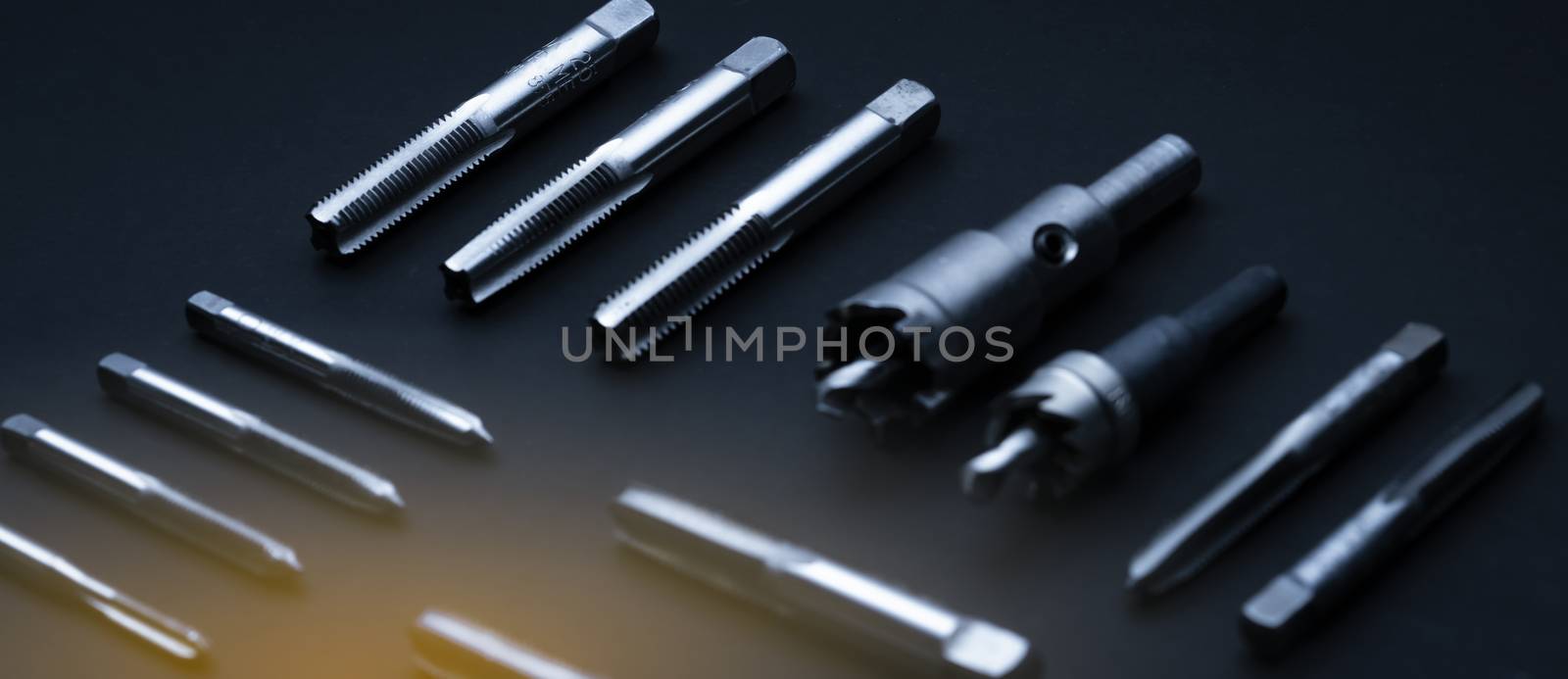 Closeup straight flute tap tip and hole saw on dark background.  Industrial tapping tools. Carbide tip metal cutter. Metalworking hardware. Mechanic tools. Drilling equipment. Mechanical engineering. 