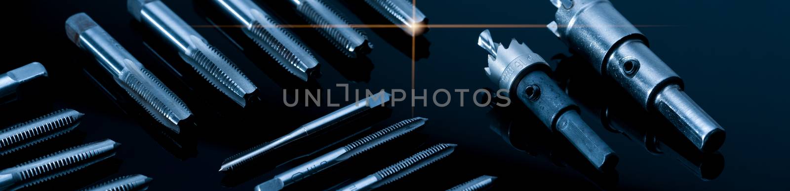 Closeup straight flute tap tip and hole saw on dark background.  Industrial tapping tools. Carbide tip metal cutter. Metalworking hardware. Mechanic tools. Drilling equipment. Mechanical engineering. 