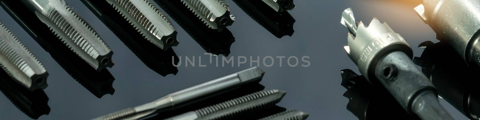 Closeup straight flute tap tip and hole saw on dark background.  by Fahroni