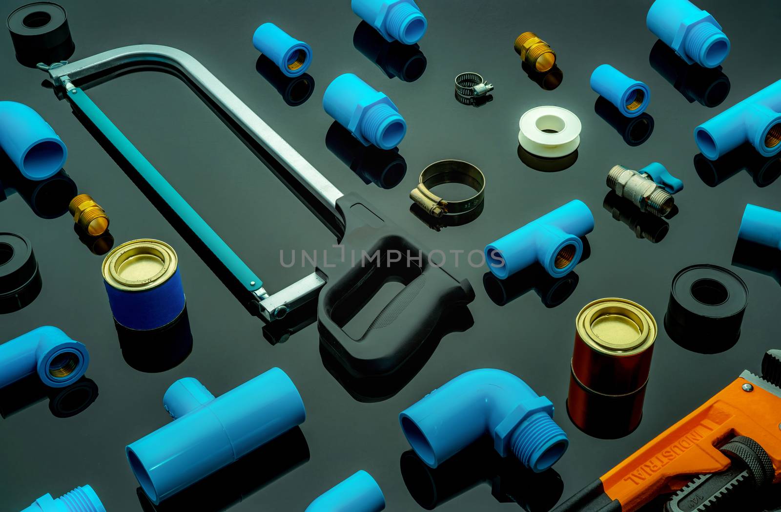 Plumbing tools. Plumber equipment. Blue PVC pipe fittings, hacksaw, glue can, and pipe wrench. House plumbing repair and maintenance service. DIY tools for plumbing work isolated on dark background. 