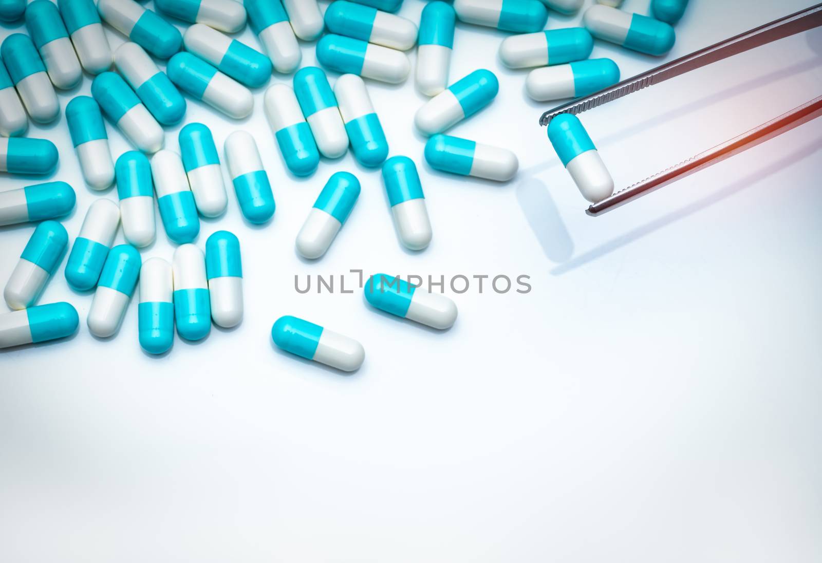 Forceps pick white-blue capsule from group of capsule pills. Drugs choose. Antibiotic drug selection. Antibiotic drug resistance concept. QA and QC in pharmaceutical factory concept. Drugs of choice.