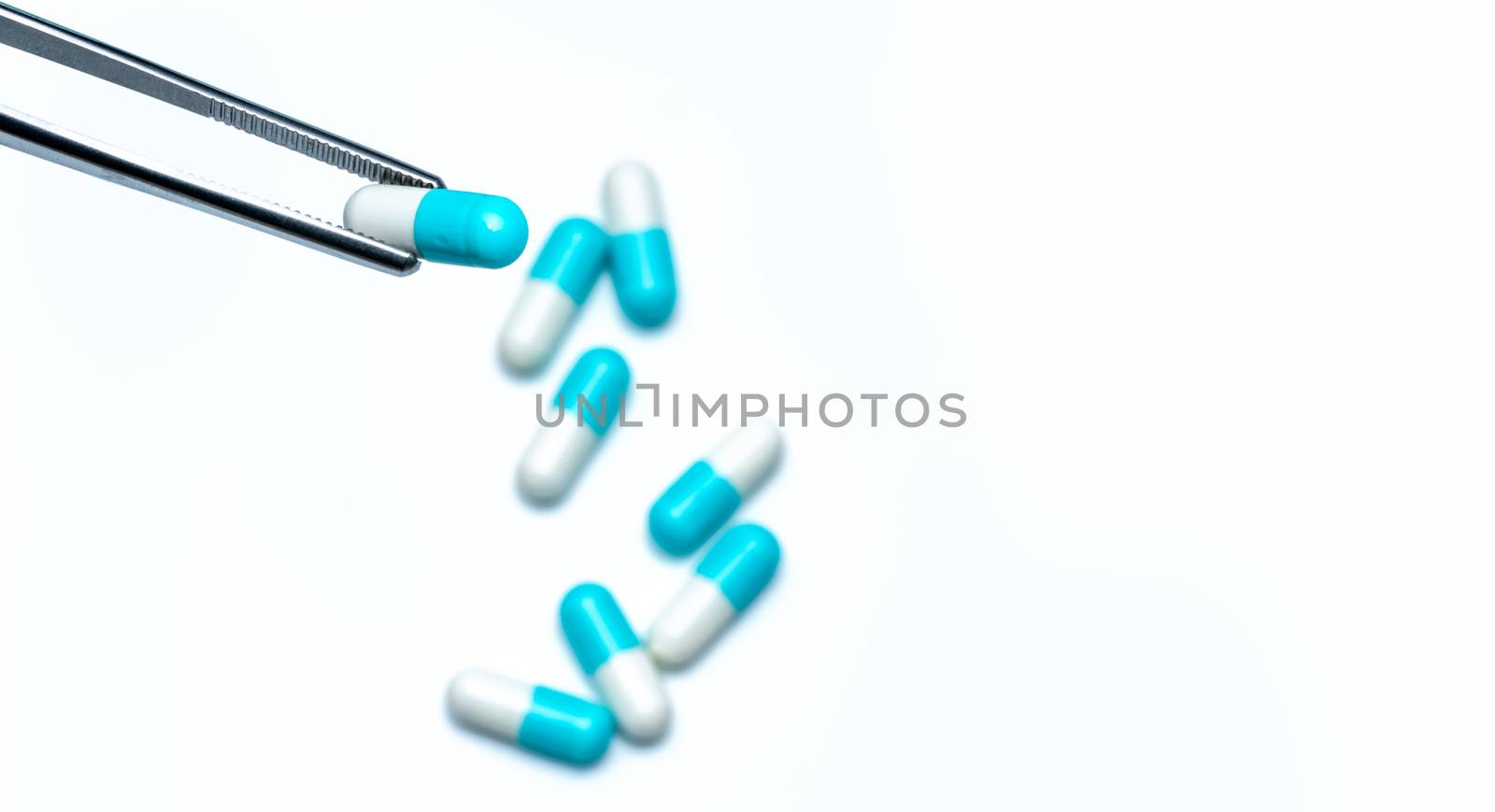 Forceps pick white-blue capsule from group of capsule pills. Drugs choose. Antibiotic drug selection. Antibiotic drug resistance concept. QA and QC in pharmaceutical factory concept. Drugs of choice.