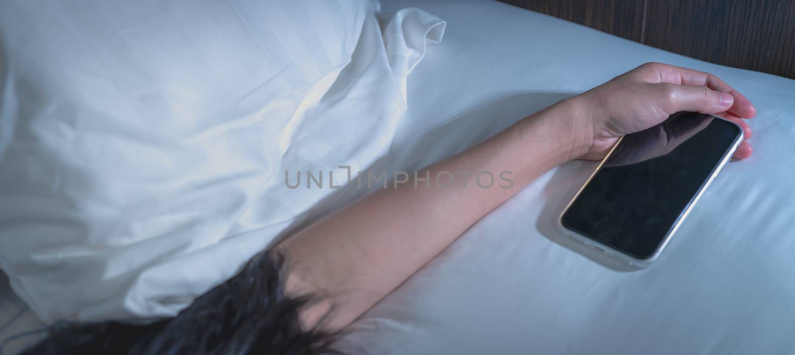 Asian woman sleeping in bed at home and hand holding mobile phone. Woman using smartphone in bedroom. Young woman addicted using smartphone. Texting on cellphone with tired until falling asleep. 