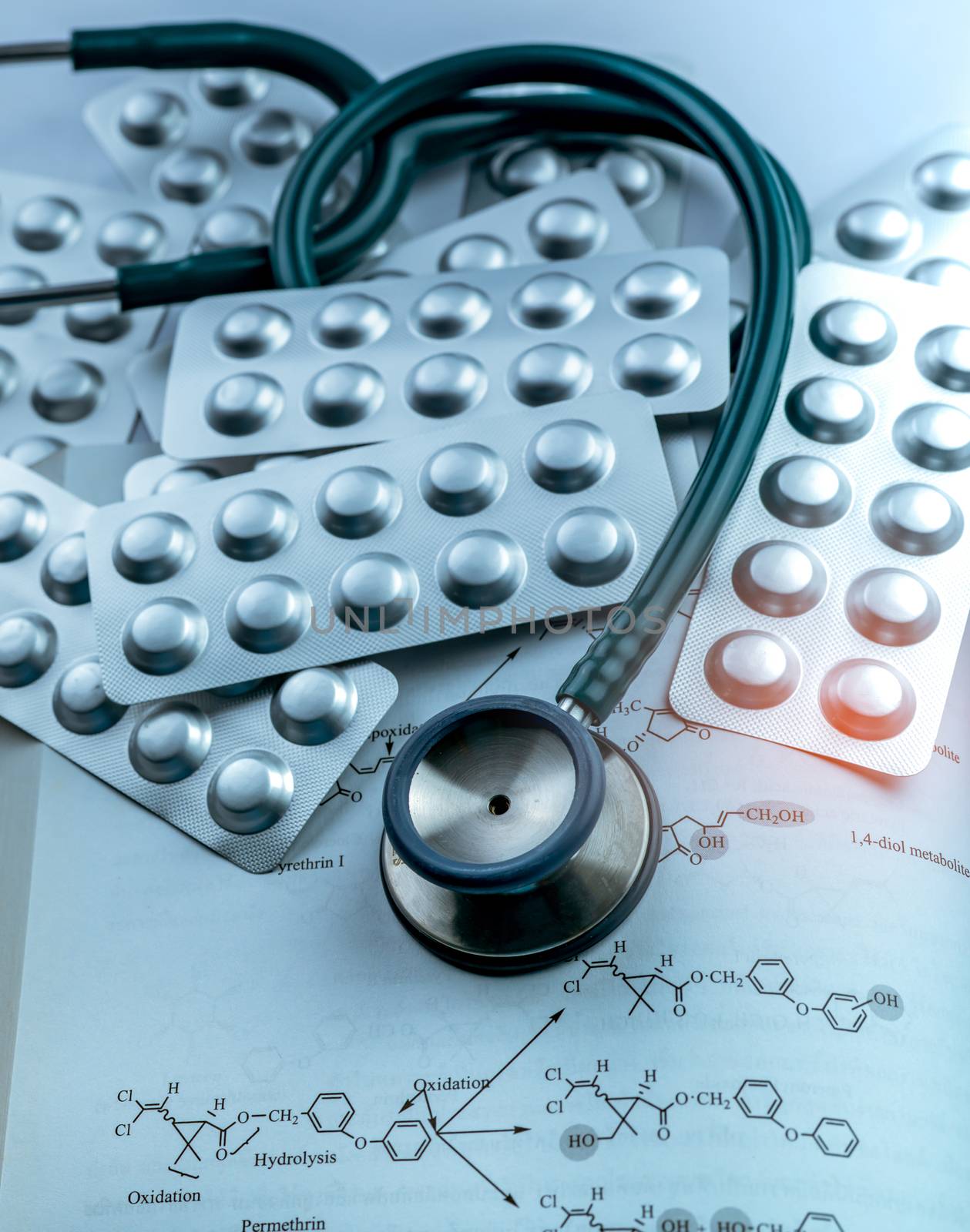 Pile of tablets pills in silver aluminium foil blister pack and stethoscope on textbook.  Pharmaceutical industry. Drug use in hospital. Healthcare. Medical diagnosis. Health checkup concept. 