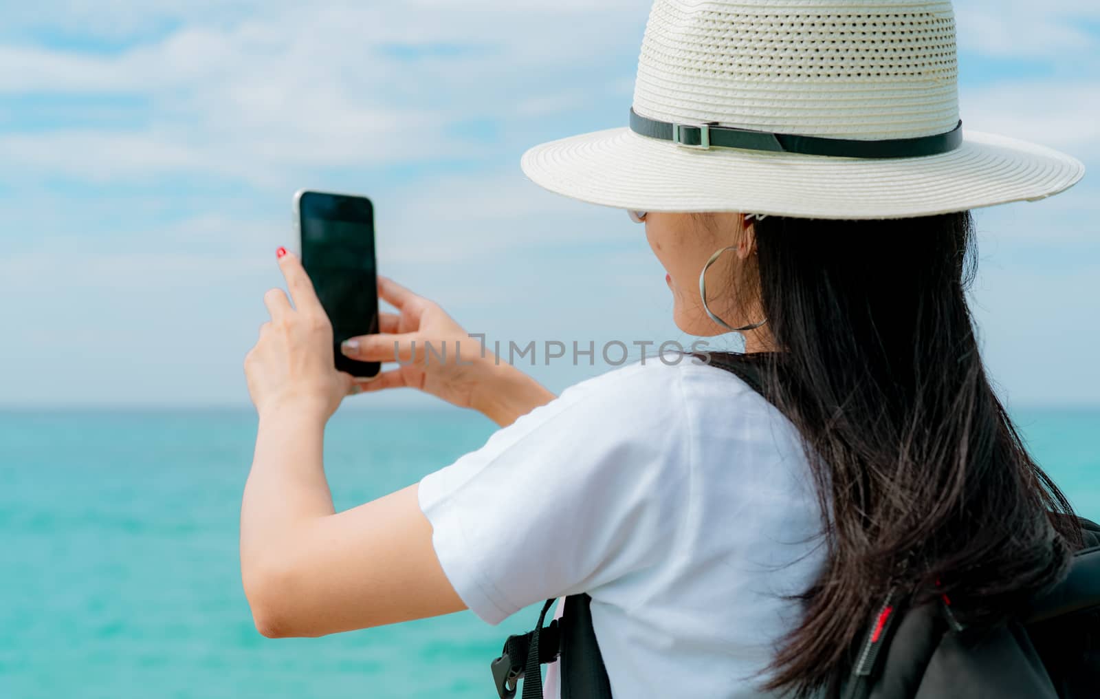 Young Asian backpacker woman wear hat use smartphone taking self by Fahroni