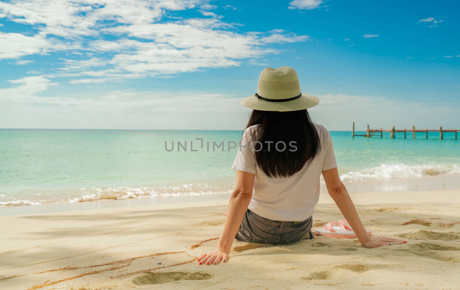 Happy young woman in white shirts and shorts sitting at sand bea by Fahroni