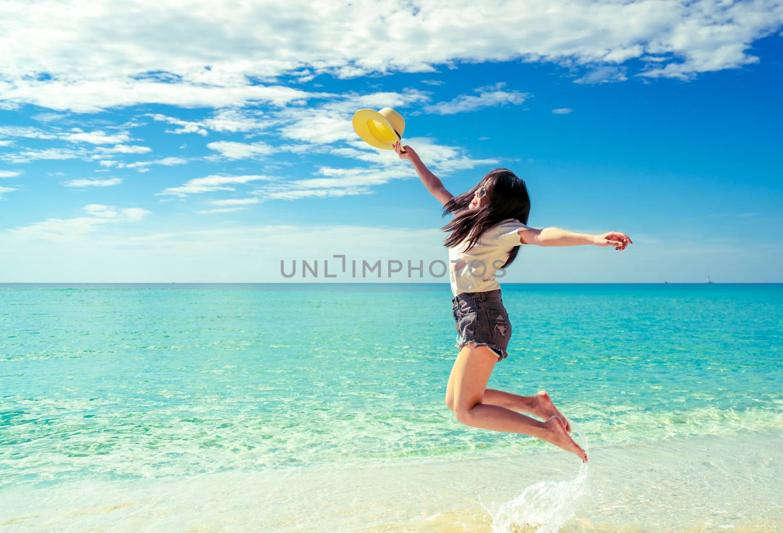 Happy young woman in casual style fashion and straw hat jumping  by Fahroni