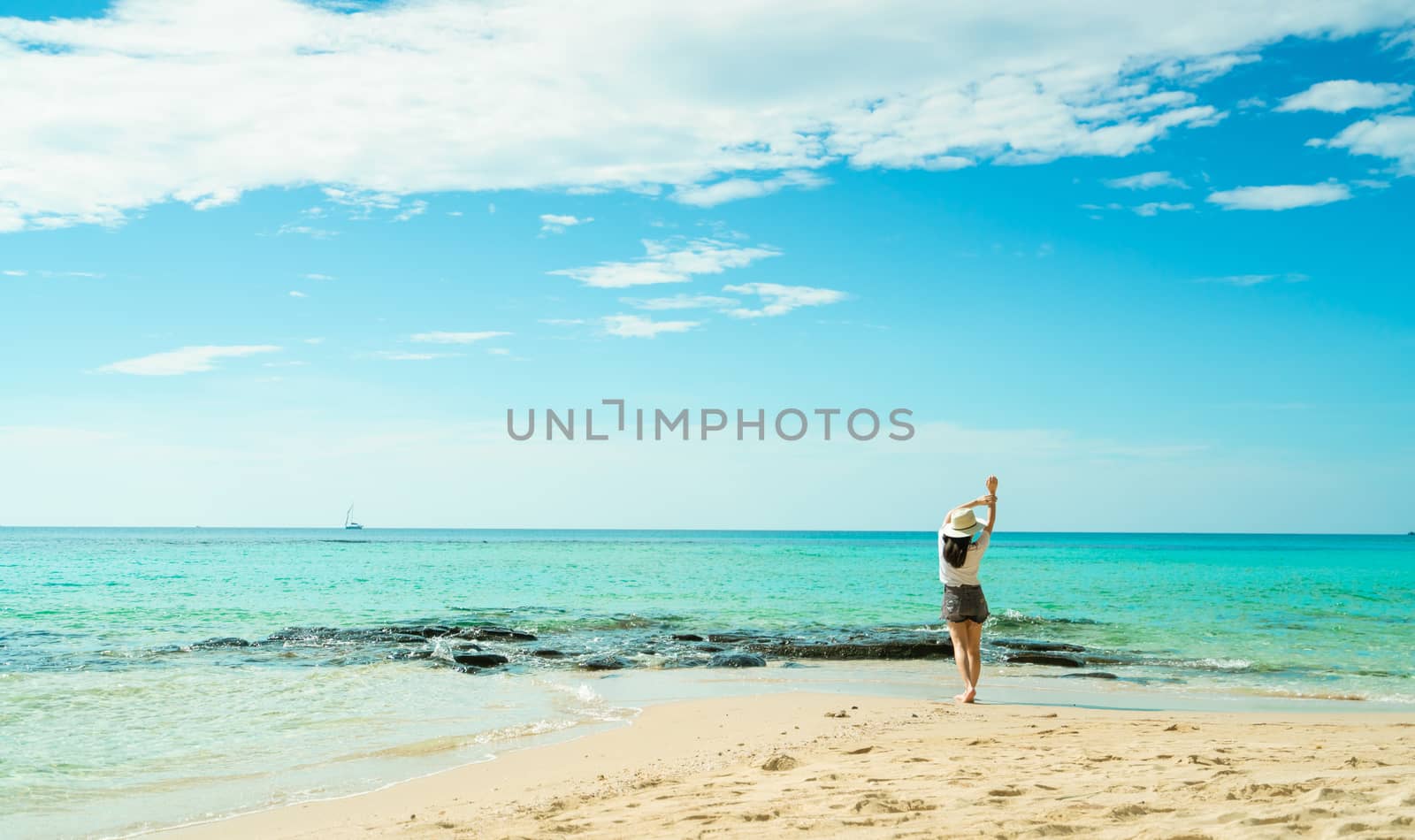 Happy young woman in white shirts and shorts walking at sand beach. Relaxing and enjoying holiday at tropical paradise beach with blue sky and clouds. Girl in summer vacation. Summer vibes. Happy day.