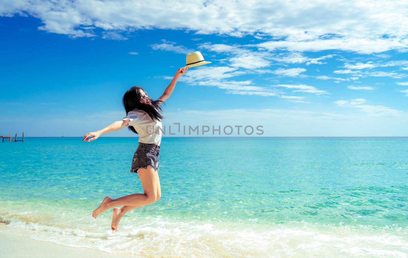 Happy young woman in casual style fashion and straw hat jumping  by Fahroni