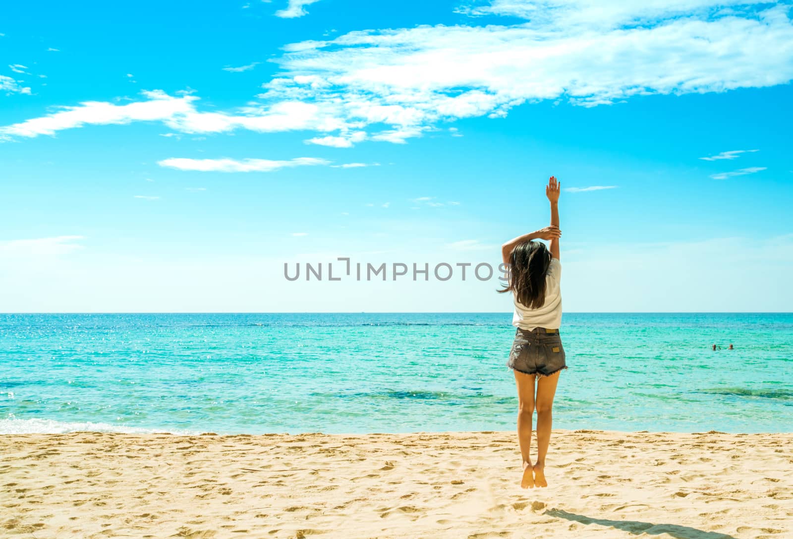 Happy young woman in white shirts and shorts jumping at sand beach. Relaxing and enjoying holiday at tropical paradise beach with blue sky and clouds. Girl in summer vacation. Summer vibes. Happy day.
