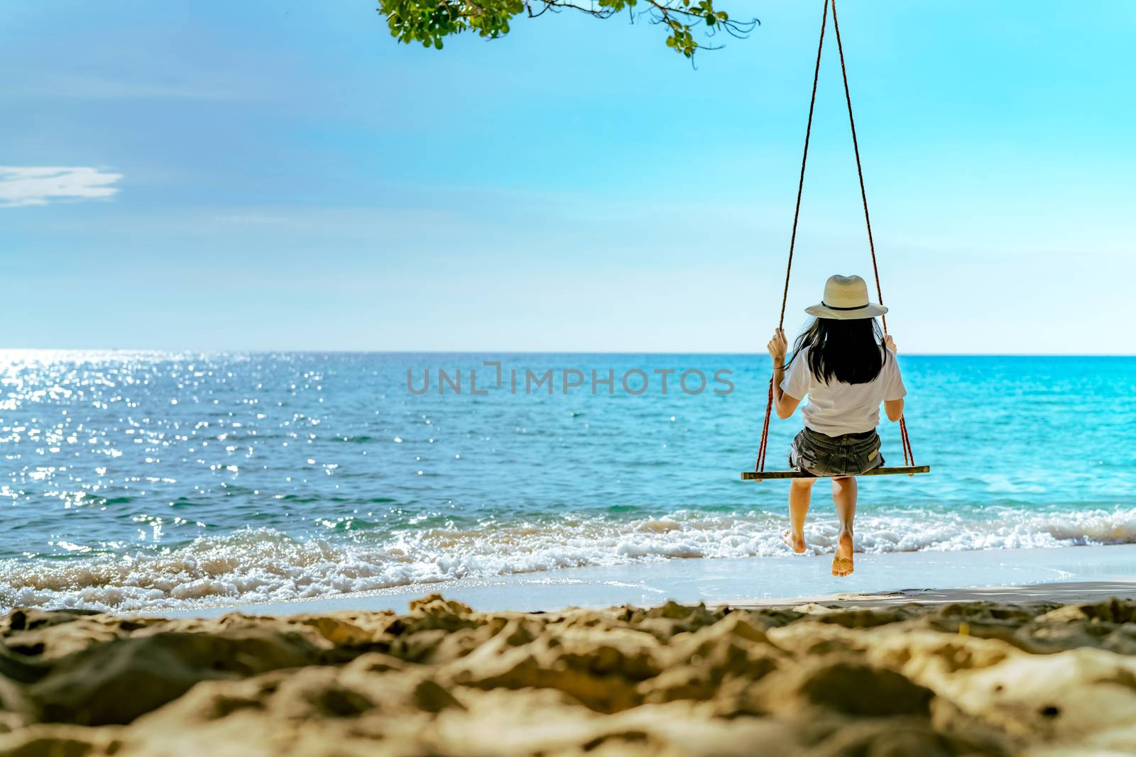 Asian woman in casual style wear hat swing the swings at sand be by Fahroni
