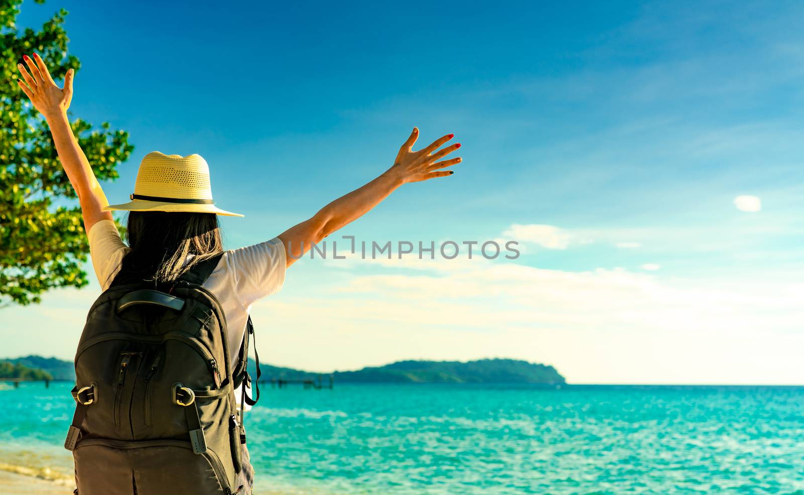 Back view of happy young Asian woman in casual style fashion with straw hat and backpack. Relax and enjoy holiday at tropical paradise beach. Summer vibes. Relaxing and enjoying at tropical beach.