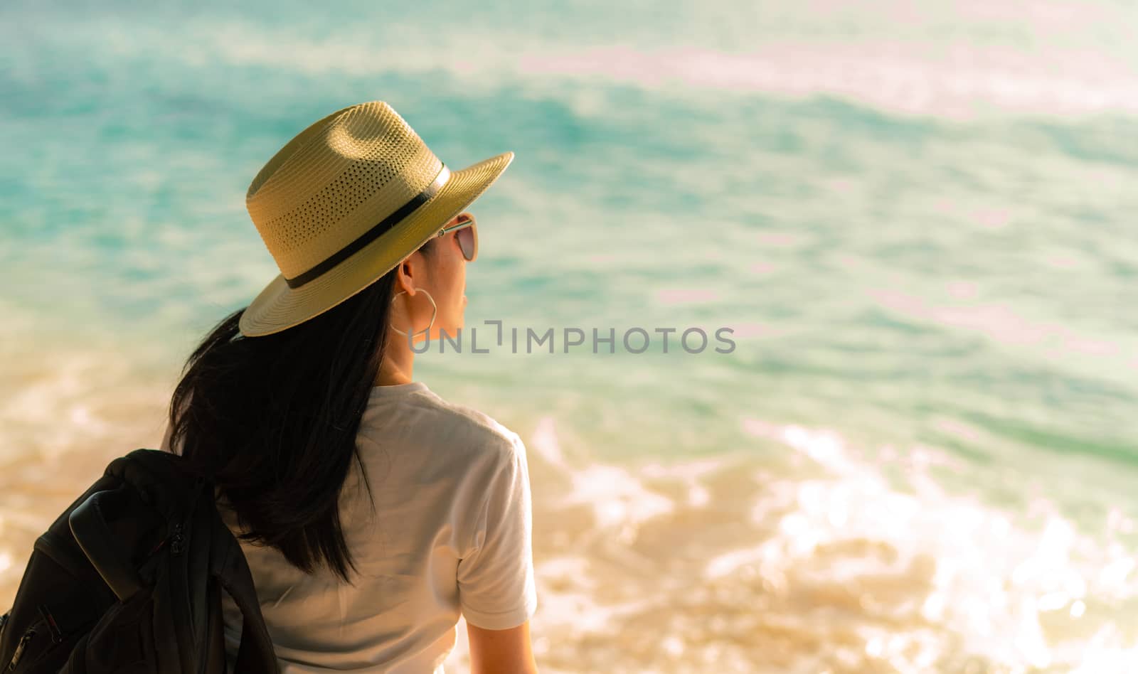 Back view of happy young Asian woman in casual style fashion with straw hat and backpack. Relax and enjoy holiday at tropical paradise beach. Summer vibes. Relaxing and enjoying at tropical beach.