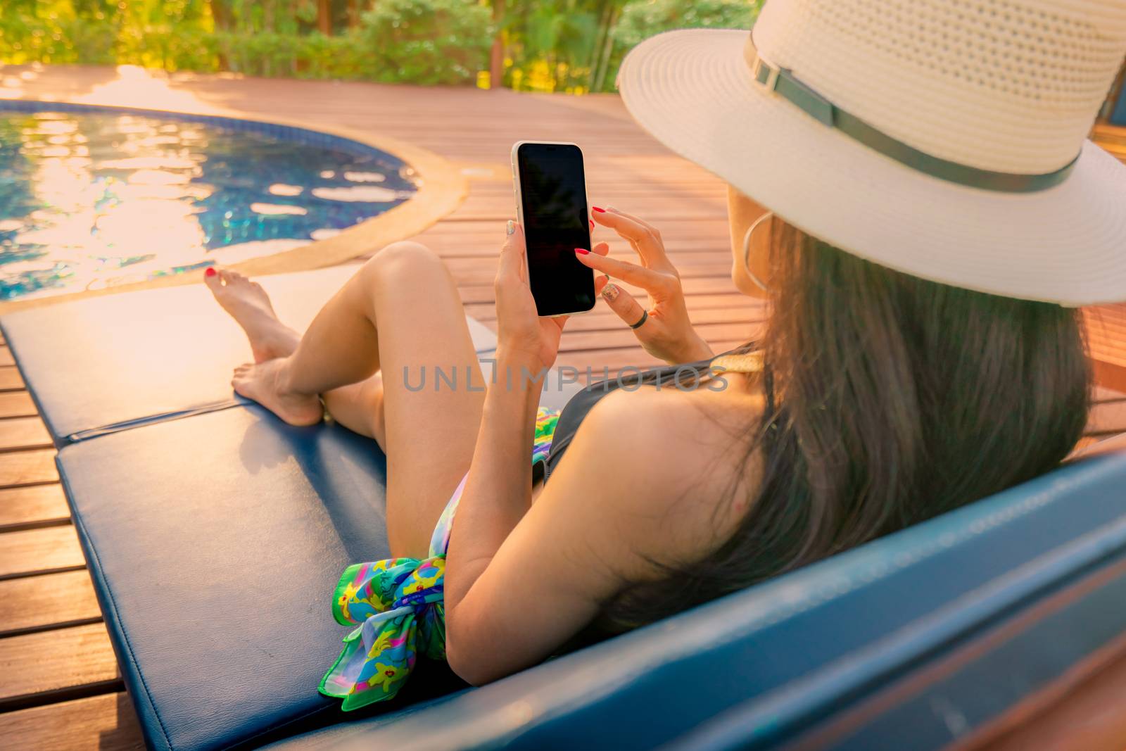 Asian woman with hat and swimsuit sitting in chair at poolside a by Fahroni