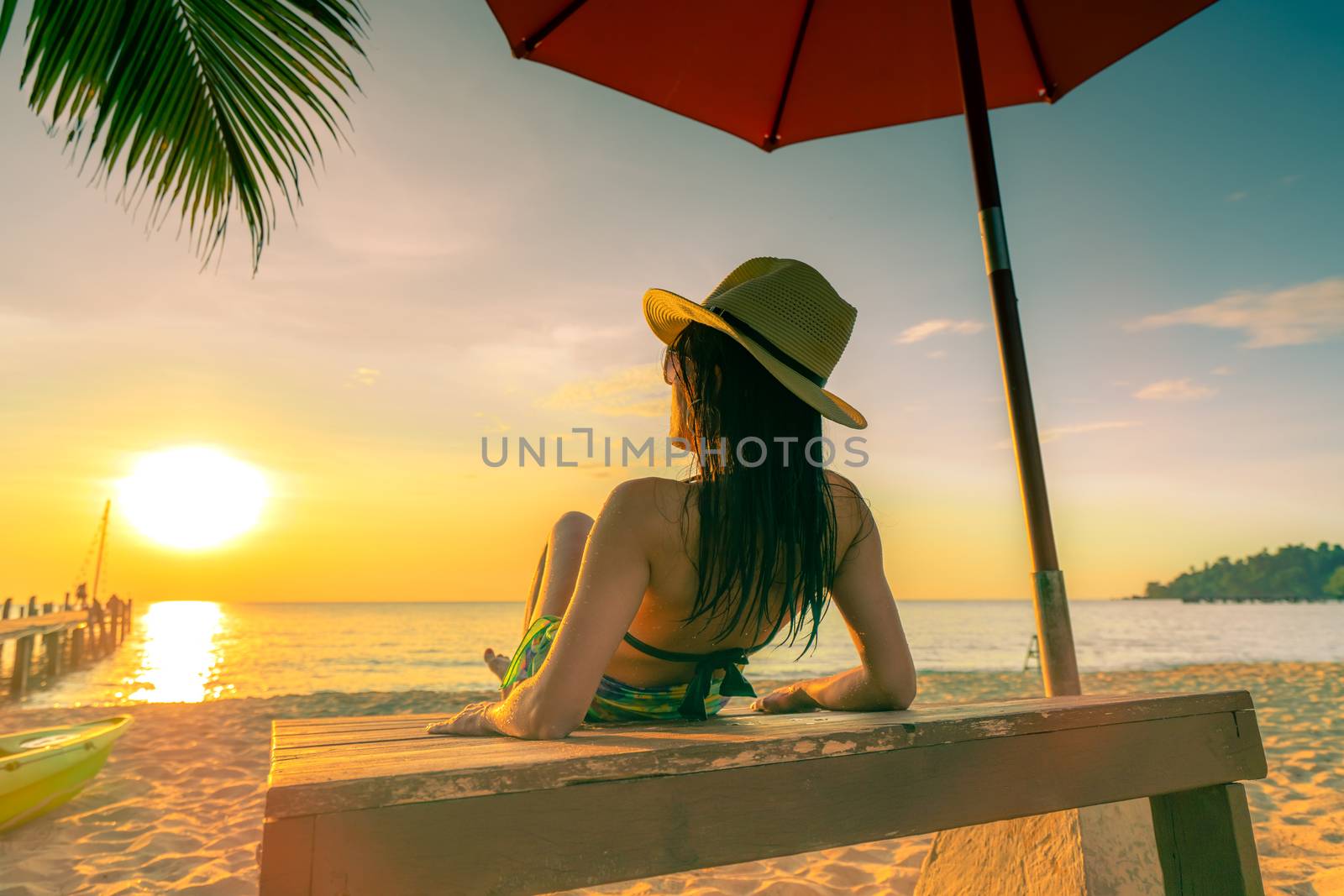 Sexy, enjoy and relax woman wear bikini lying and sunbathing on sunbed at sand beach at paradise tropical island under beach umbrella at sunset. Summer vacation. Holiday travel. Summer vibes.