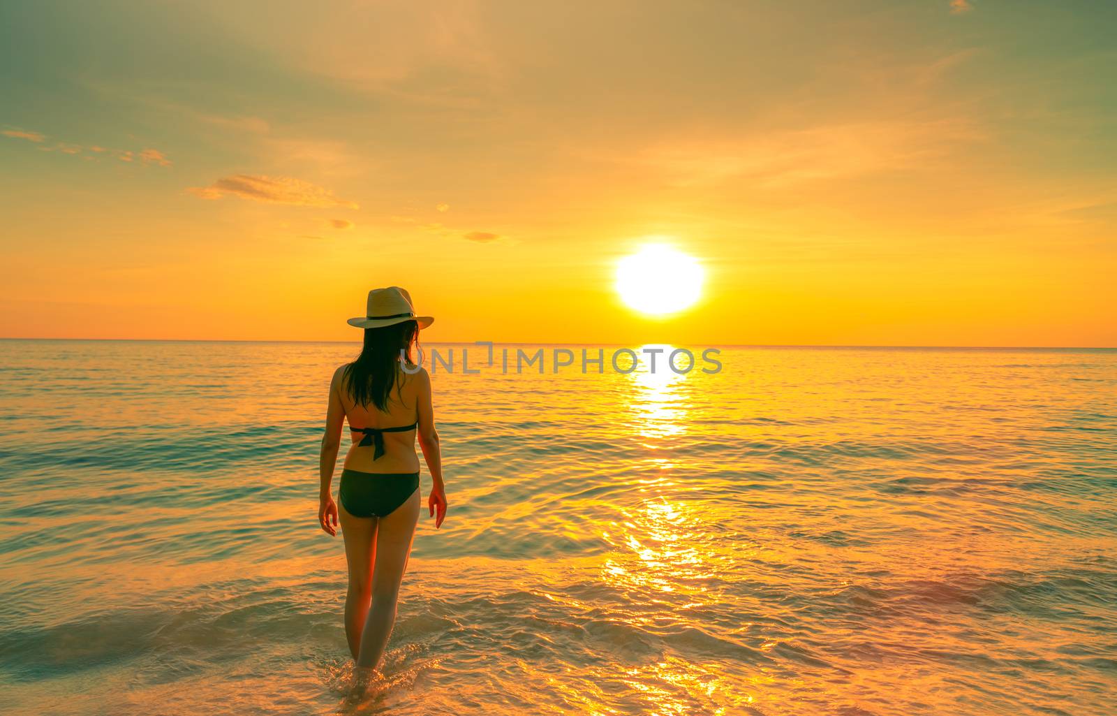 Silhouette sexy woman walking at tropical sea with beautiful sunset sky at paradise beach. Happy girl wear bikini and straw hat relaxing summer vacation. Holiday travel. Summer vibes. Life goes on.