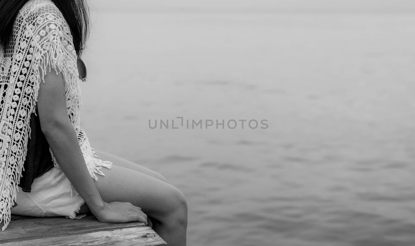 Pensive lonely adult Asian woman. Back view of woman with sad feeling in black and white scene at the sea. Depressed and stressed girl sit on wooden pier at the sea. Hopeless and despair. Suicide  