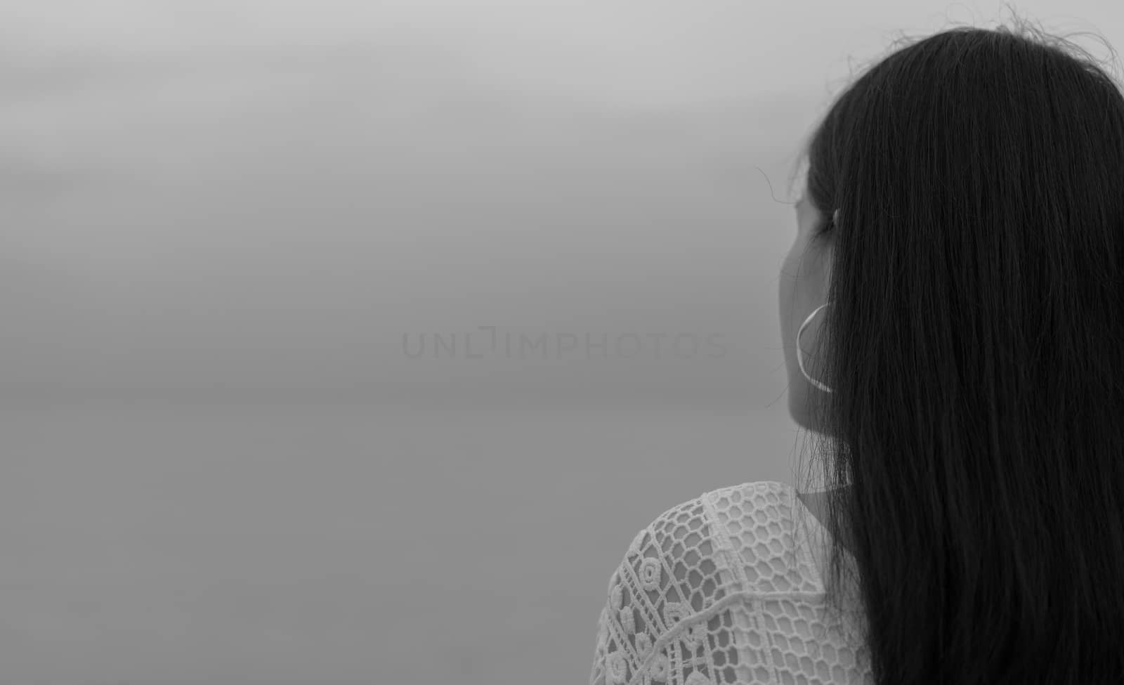 Pensive lonely young Asian woman. Back view of woman with sad feeling in black and white scene at the sea. Depressed and stressed girl stand and looking to grey sky and sea. Hopeless and despair.  