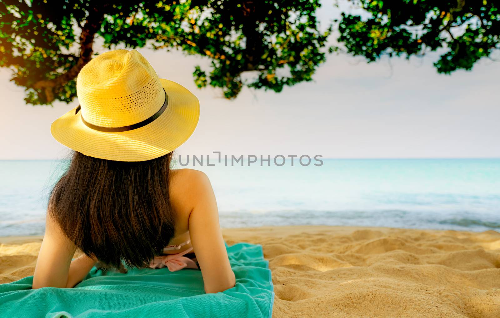 Back view of happy young Asian woman in pink swimsuit and straw hat relax and enjoy holiday at tropical sand beach under the tree. Girl in summer vacation fashion. Beauty sexy model. Summer vibes.