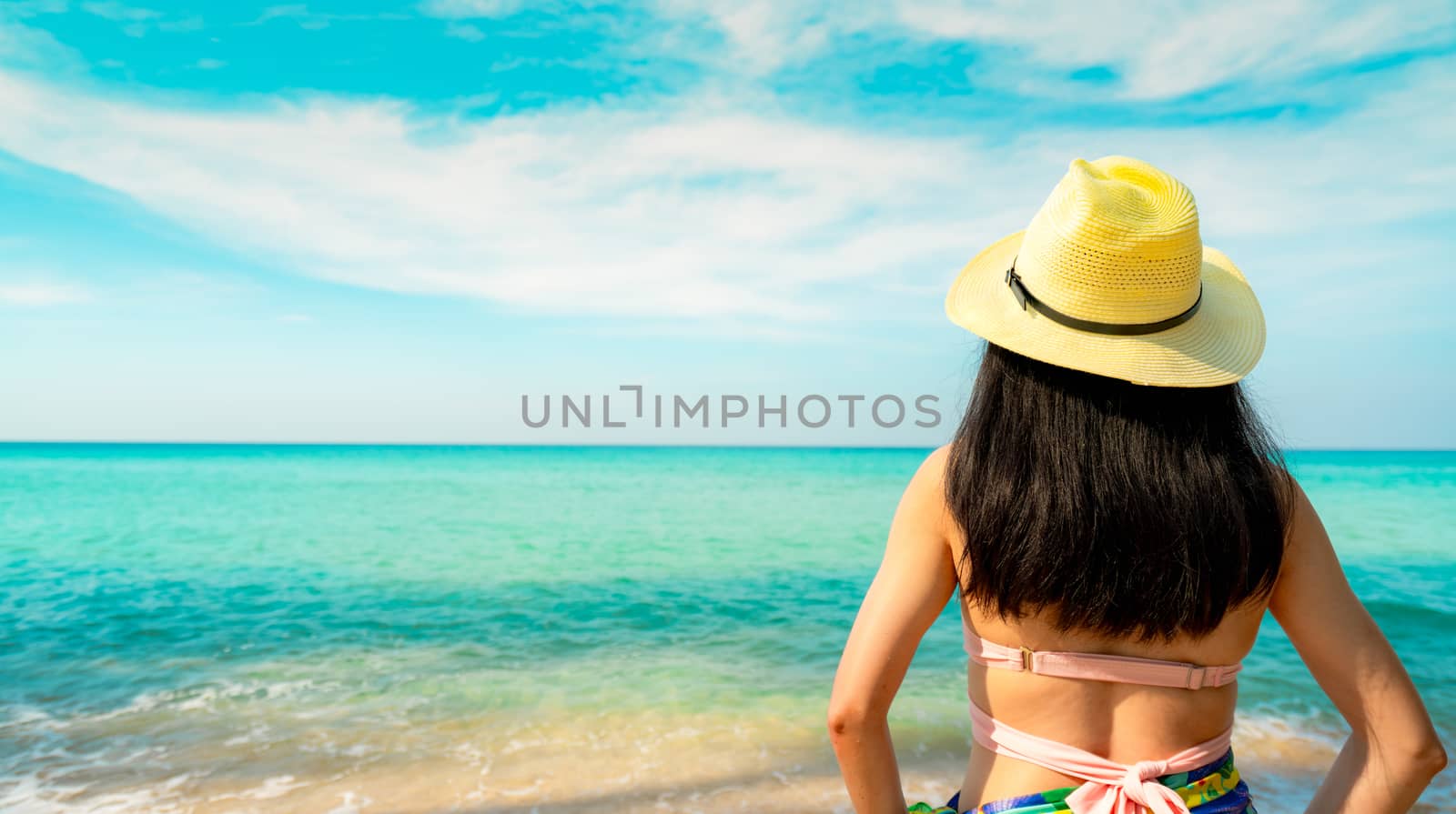 Back view of happy young Asian woman with straw hat relax and enjoy holiday at tropical paradise beach. Girl in summer vacation fashion. Beauty sexy model. Sand beach. Summer vibes. Summer travel.