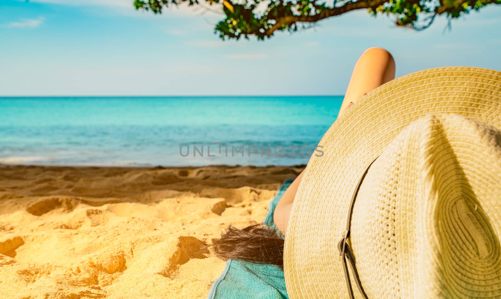 Woman lie down on green towel that put on sand beach under the tree and reading a book. Slow life on summer vacation. Asian woman with hat relaxing and enjoying holiday at tropical beach. Summer vibes