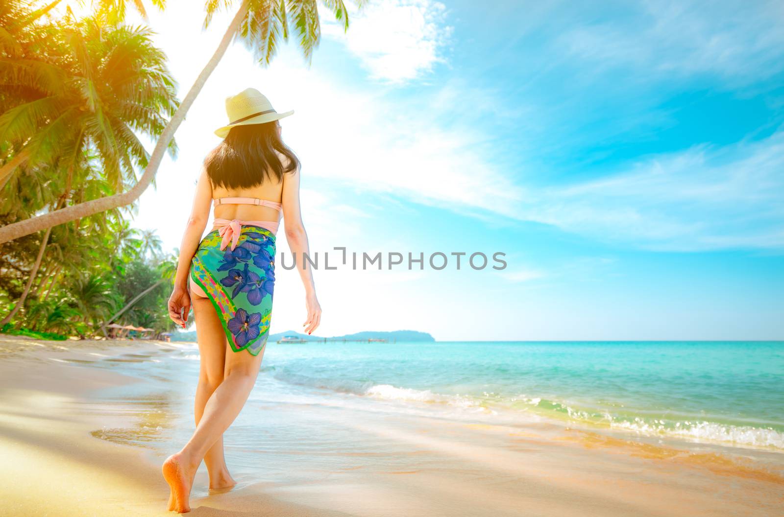 Back view of happy young Asian woman in pink swimsuit and straw hat relax and enjoy holiday at tropical paradise beach. Girl in summer vacation fashion. Beauty sexy model. Sand beach and coconut tree.
