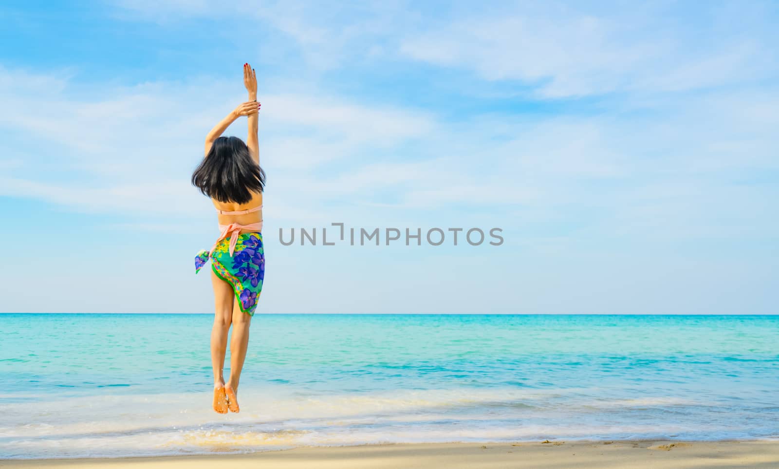 Happy young woman in swimsuit jumping at sand beach. Relaxing and enjoying holiday at tropical paradise beach with blue sky and clouds. Girl in summer vacation. Summer vibes. Happy day. Travel alone.