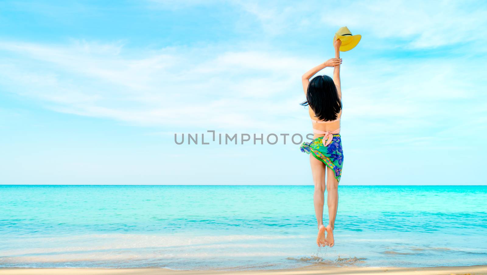 Happy young woman in pink swimwear hand holding hat and jumping  by Fahroni