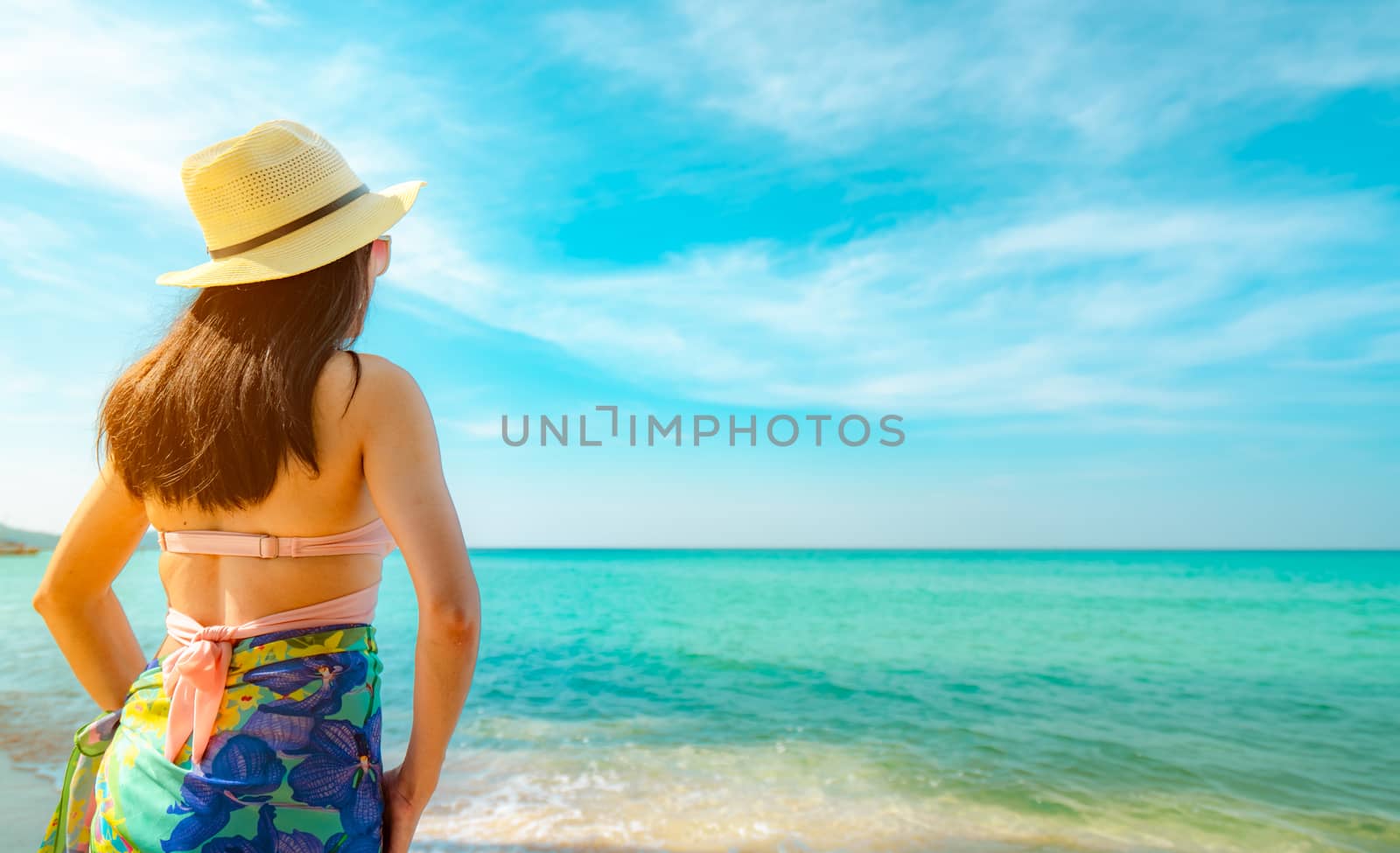 Back view of happy young Asian woman with straw hat relax and enjoy holiday at tropical paradise beach. Girl in summer vacation fashion. Beauty sexy model. Sand beach. Summer vibes. Summer travel.