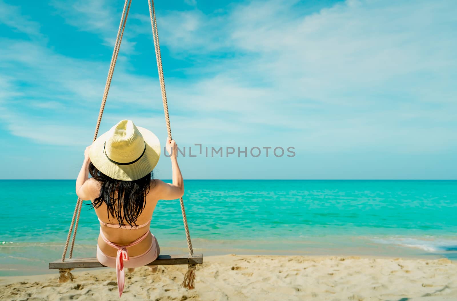 Asian woman wear swimwear and hat swing the swings at sand beach by Fahroni