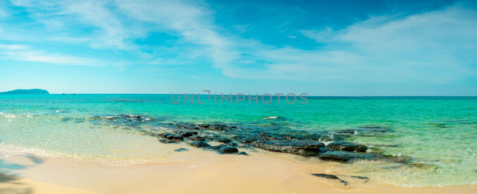 Golden sand beach by the sea with emerald green sea water and blue sky and white clouds. Summer vacation on tropical paradise beach concept. Ripple of water splash on sandy beach. Summer vibes. 