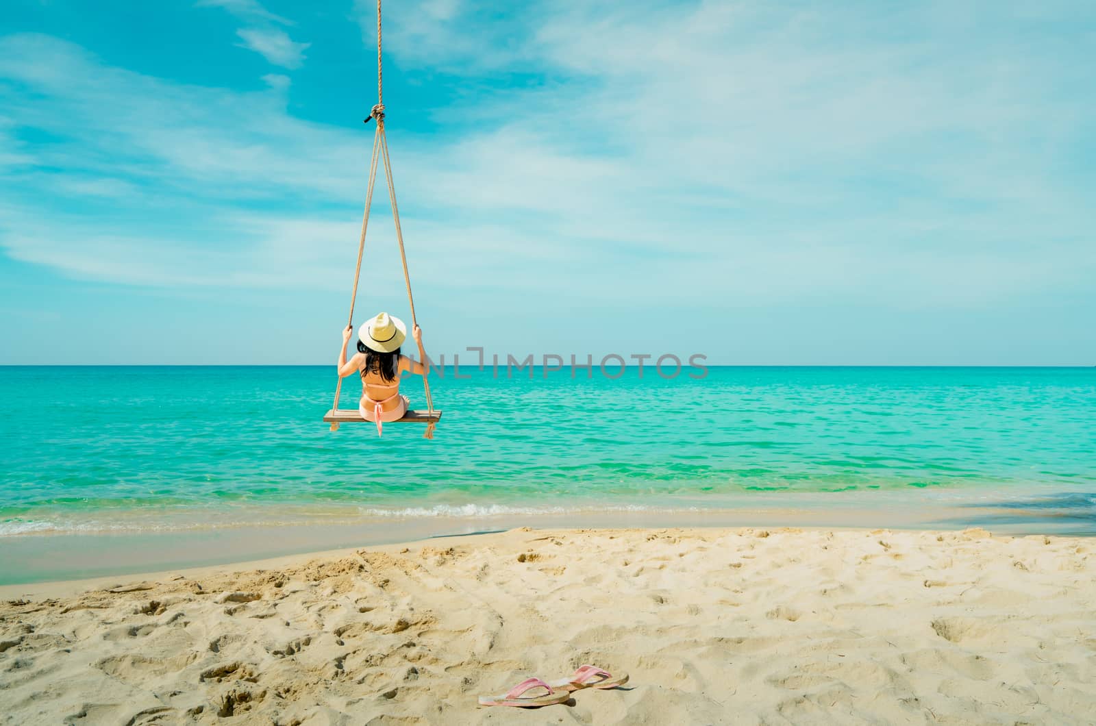 Asian woman wear swimwear and hat swing the swings at sand beach by Fahroni