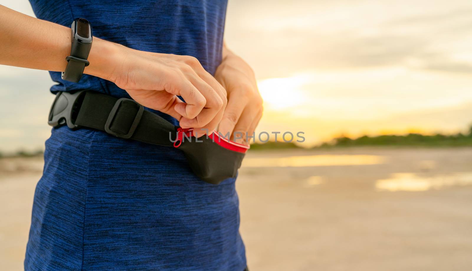 Young Asian woman keep smartphone in waist bag before running ca by Fahroni