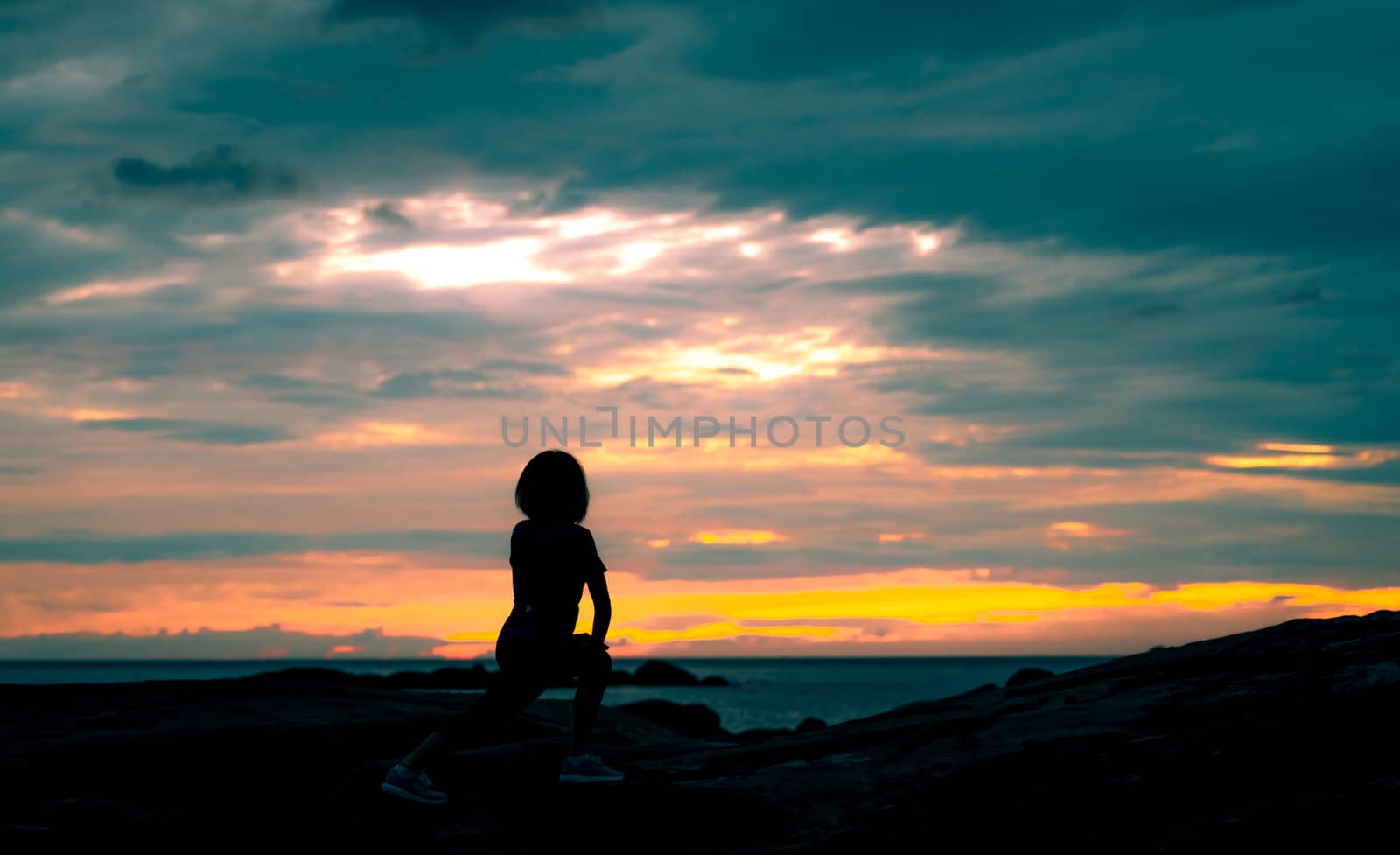 Silhouette woman workout in the morning at stone beach with beautiful sunrise sky. Fit woman stretching body before workout. Exercise for healthy lifestyle. Out door workout. Nature landscape. Freedom