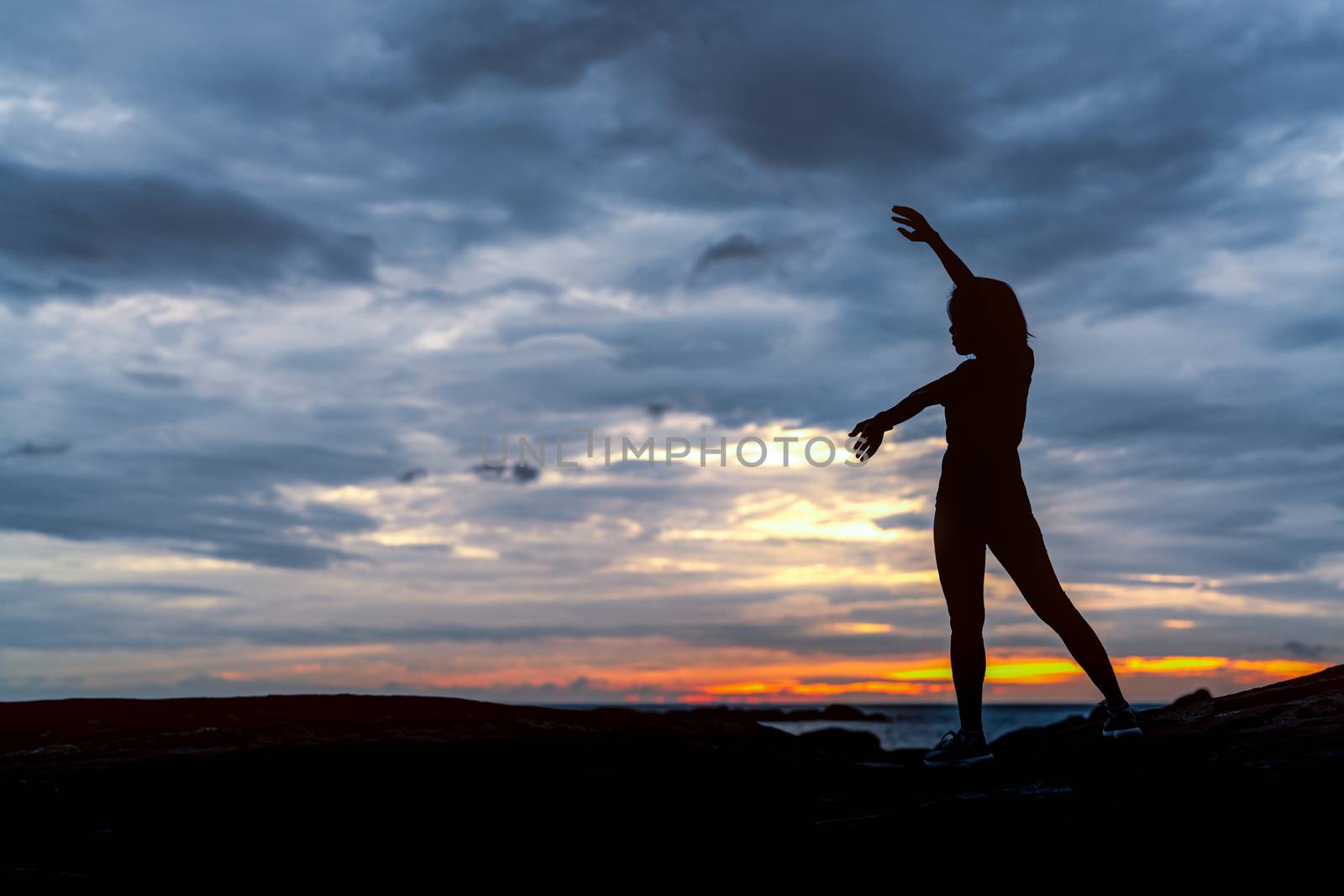 Silhouette woman workout in the morning at stone beach with beautiful sunrise sky. Fit woman stretching body before workout. Exercise for healthy lifestyle. Out door workout. Nature landscape. Freedom