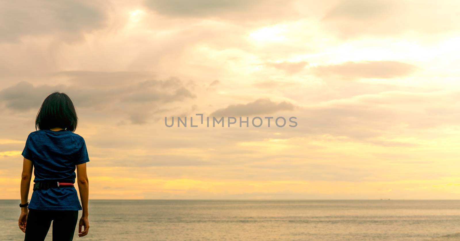 Asian woman watching sunrise sky at sea beach. Runner relax afte by Fahroni