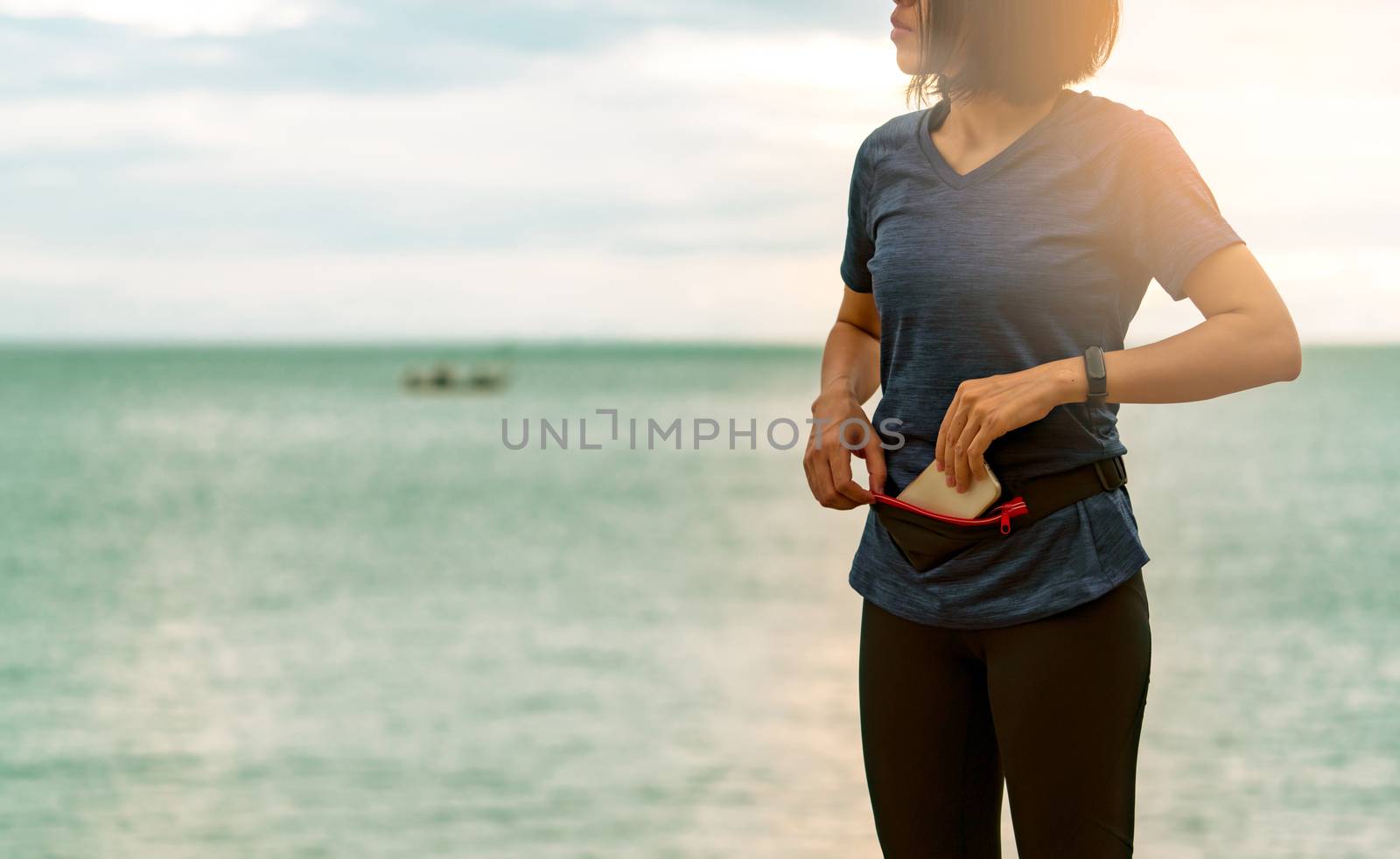 Young Asian woman keep smartphone in waist bag before running ca by Fahroni