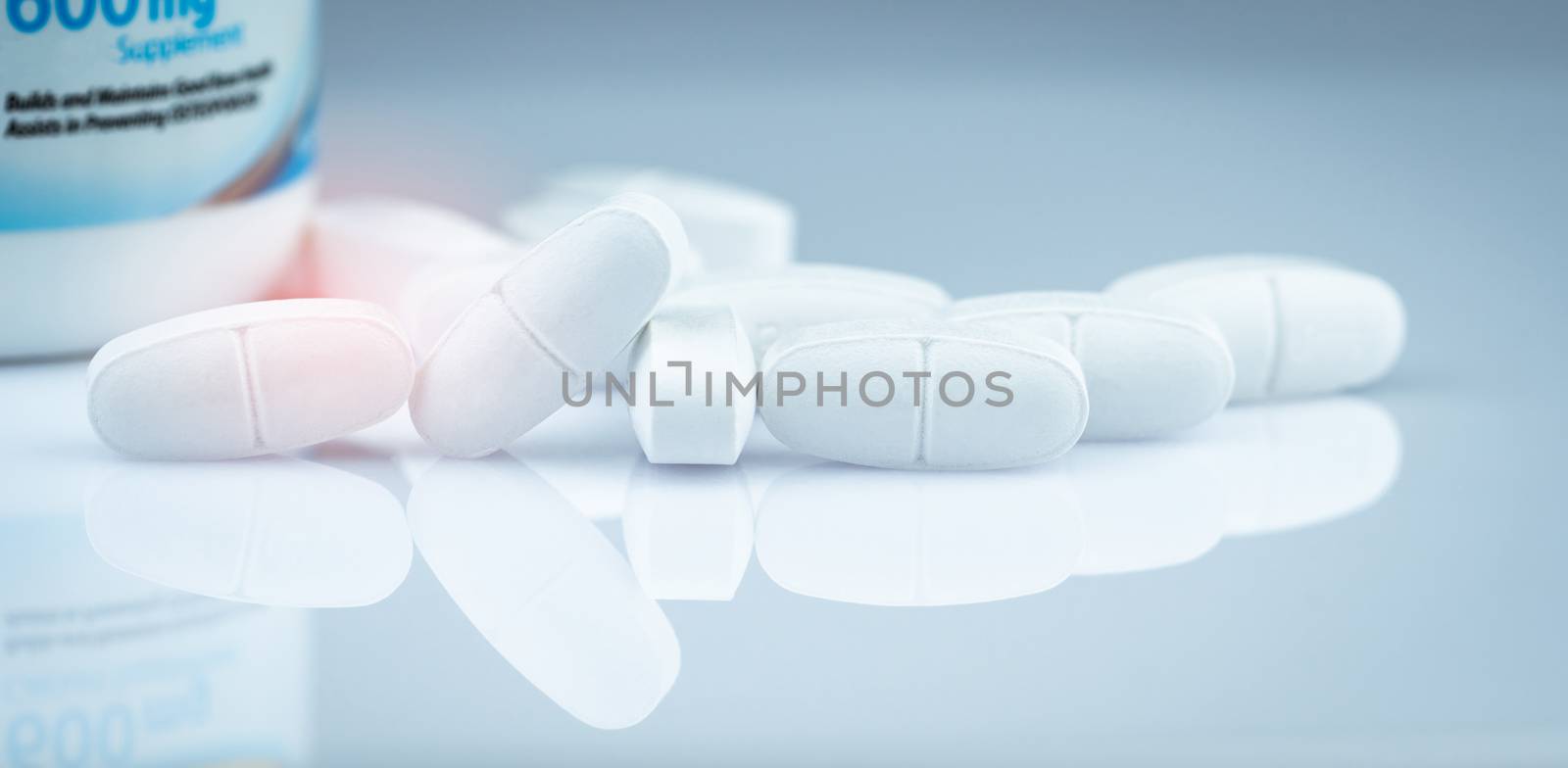 Calcium tablets for children or pregnant woman. White tablets pills on blurred drug bottle background. Vitamins and supplement concept. Pharmaceutical industry. Pharmacy products. Global healthcare.