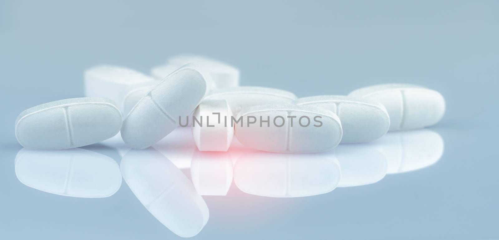 Pile of white oblong tablets pills on gradient background. White antibiotic tablet pills. Pharmaceutical industry. Pharmacy product. Drug in pharmacy drugstore or hospital. Antibiotic drug resistance.