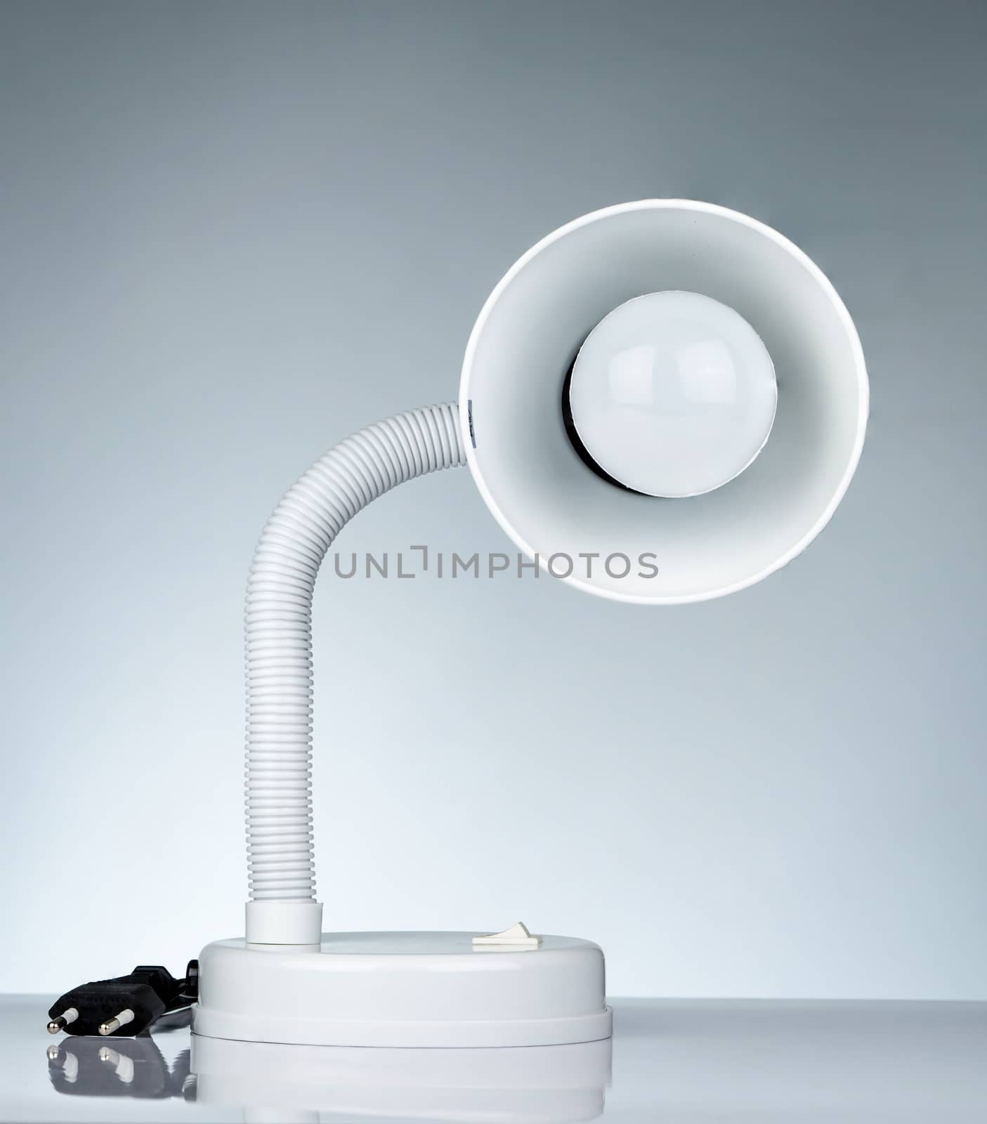 White modern table lamp isolated on white table on gradient background. Desk lamp for reading a book in dormitory room. Home and office furniture with minimalist design. Desk spotlight.