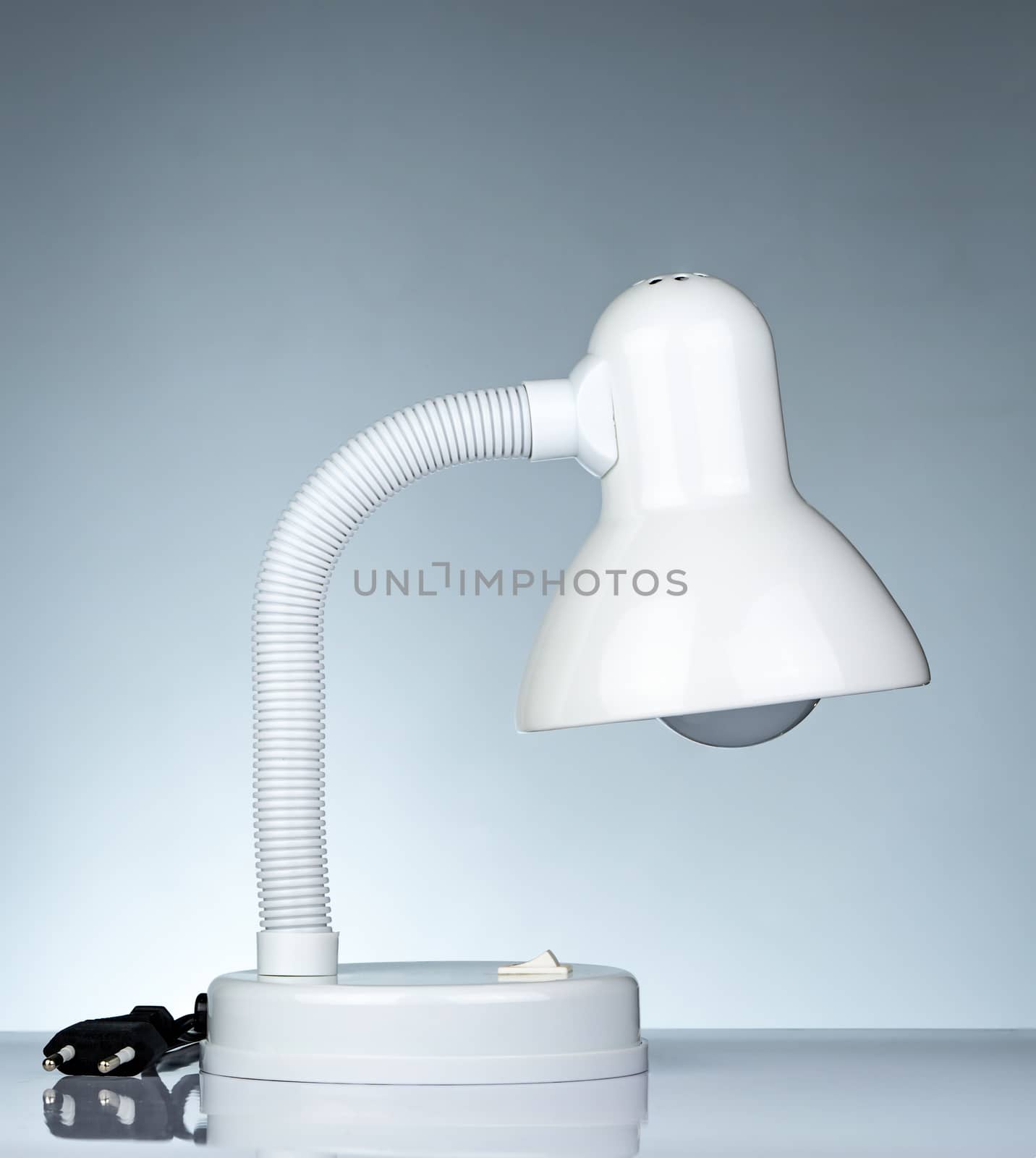 Unplugged white modern table lamp isolated on white table on gradient background. Desk lamp for reading a book in dormitory room. Home and office furniture with minimalist design. Desk spotlight.